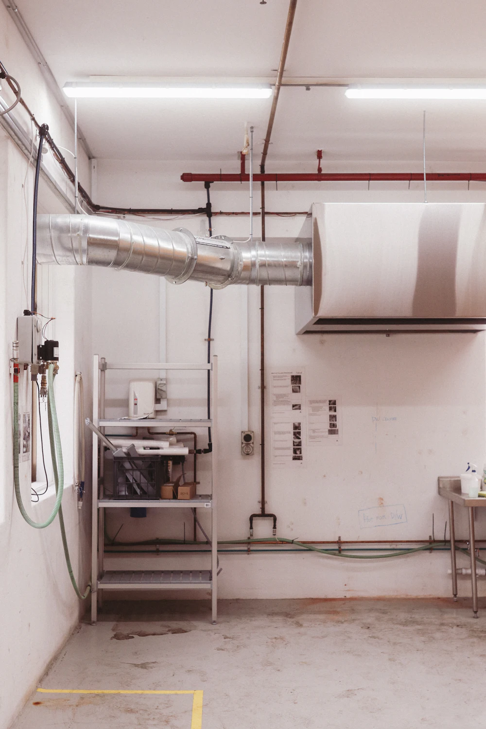 Industrial ventilation ducts and red pipes over a work area