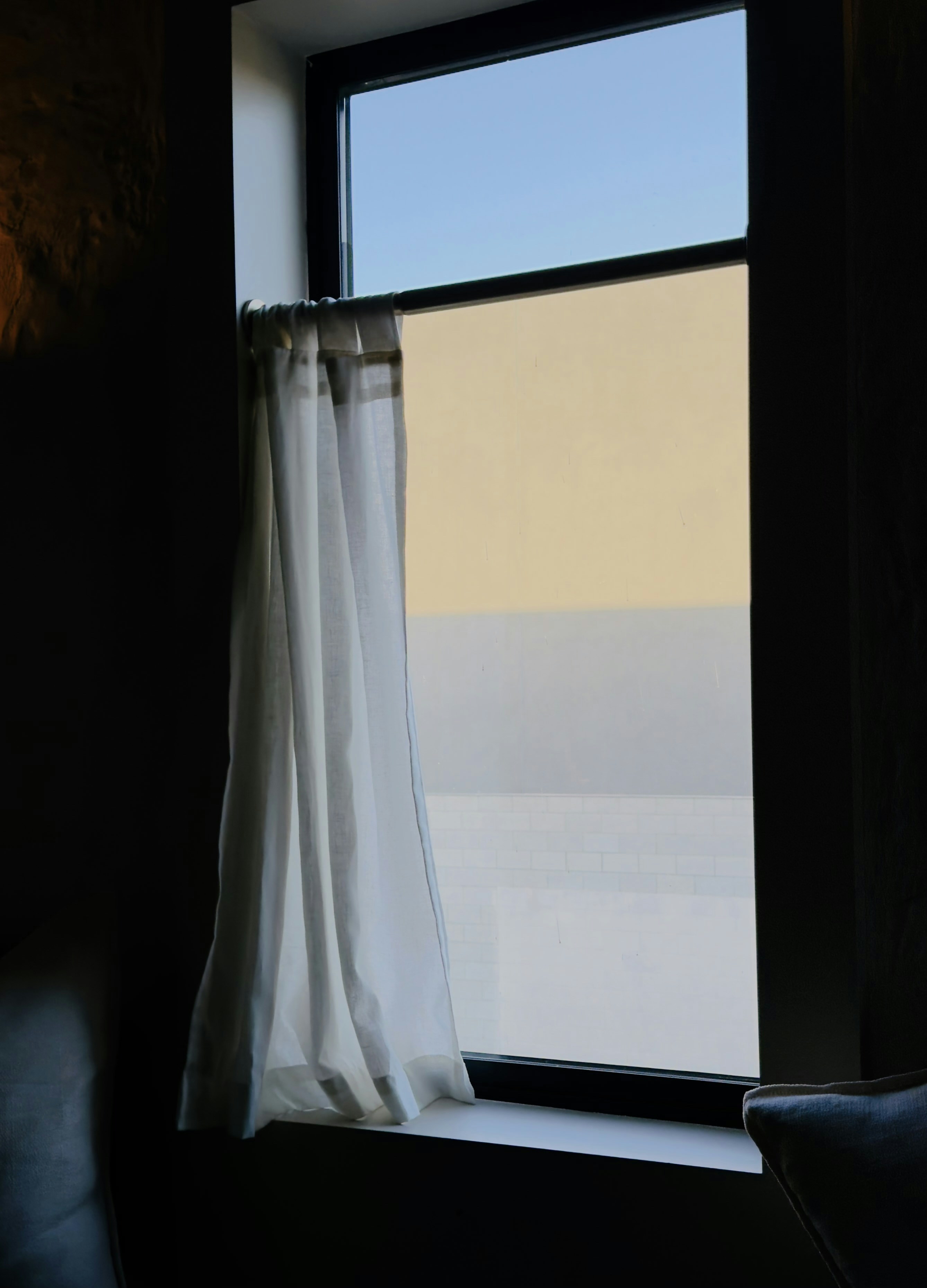 La fenêtre au rideau blanc révèle un ciel bleu et des vitres givrées.