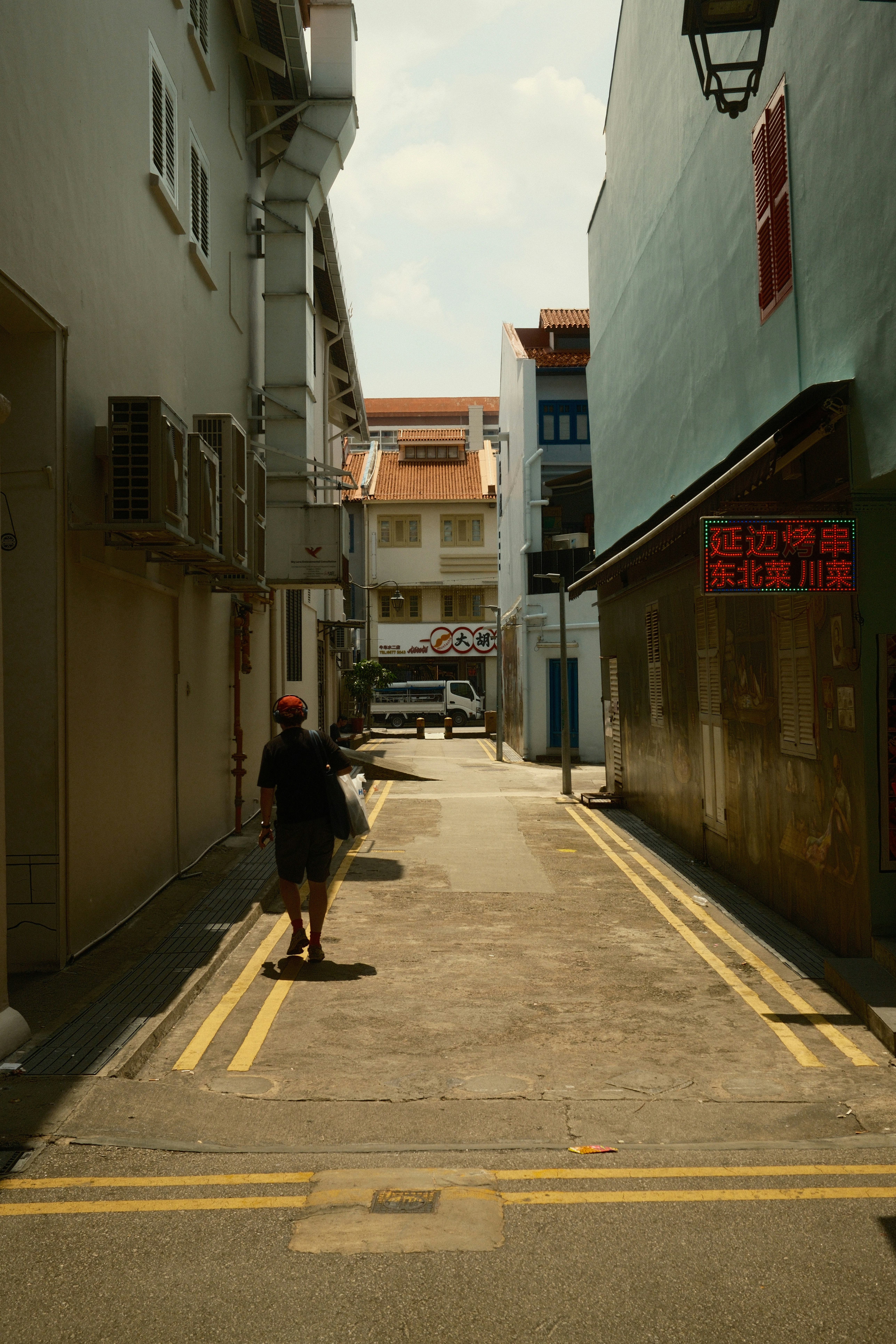 A person walks down a sunlit urban alleyway.