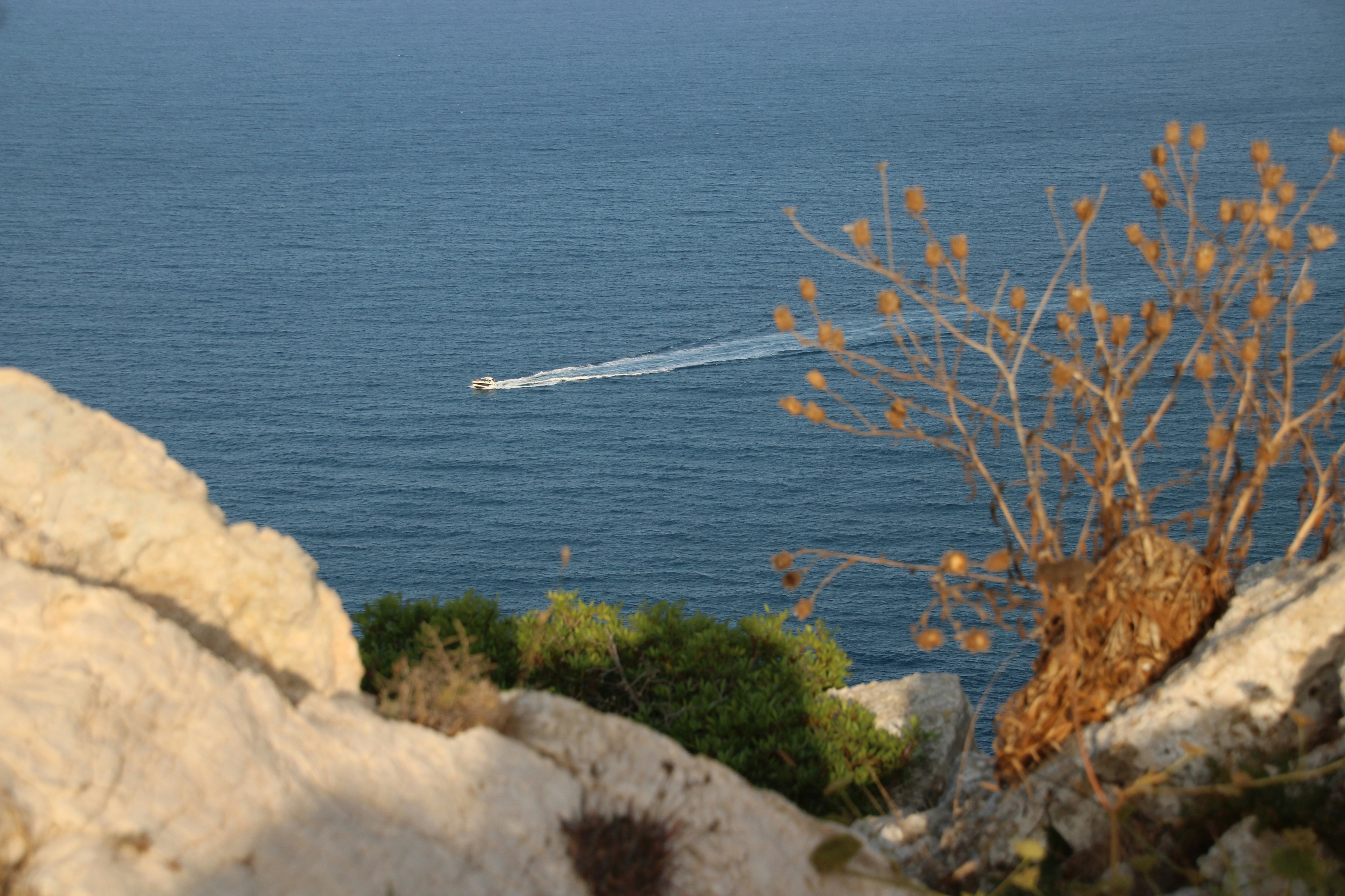 Barca sull'oceano blu, vista da una scogliera rocciosa.