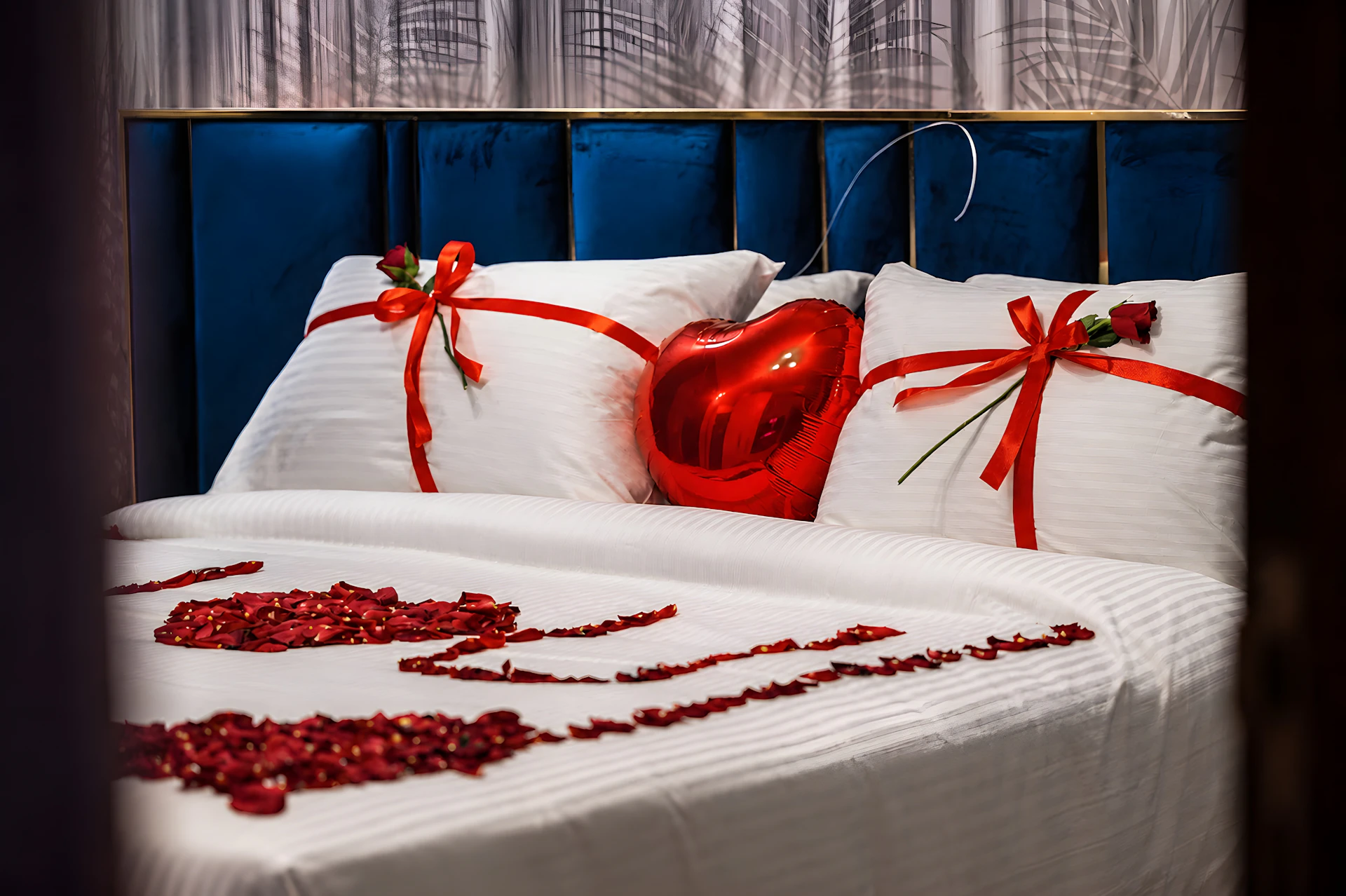A bed decorated with red rose petals and heart-shaped items