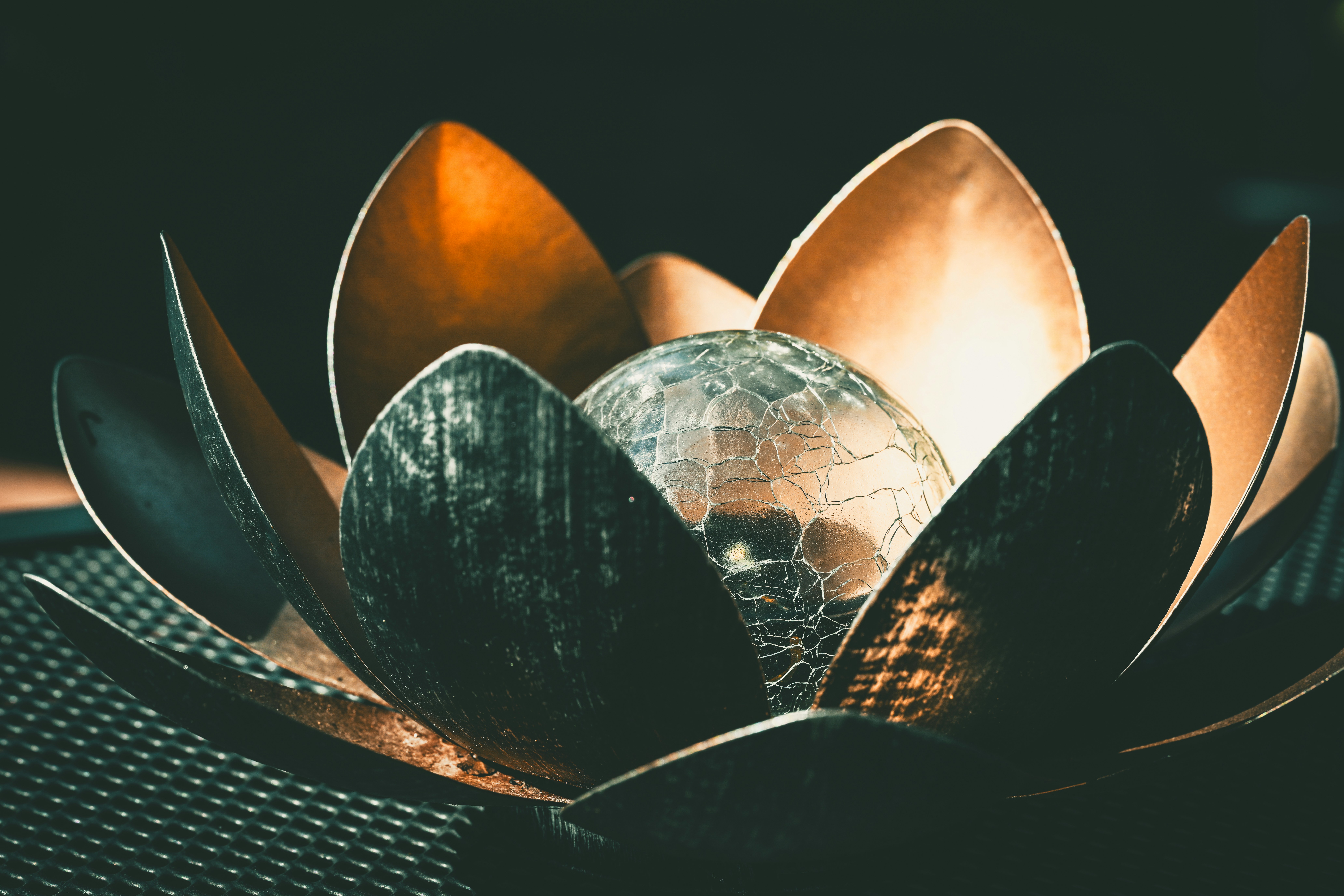 Uma escultura metálica de flor de lótus com uma esfera de vidro rachada.