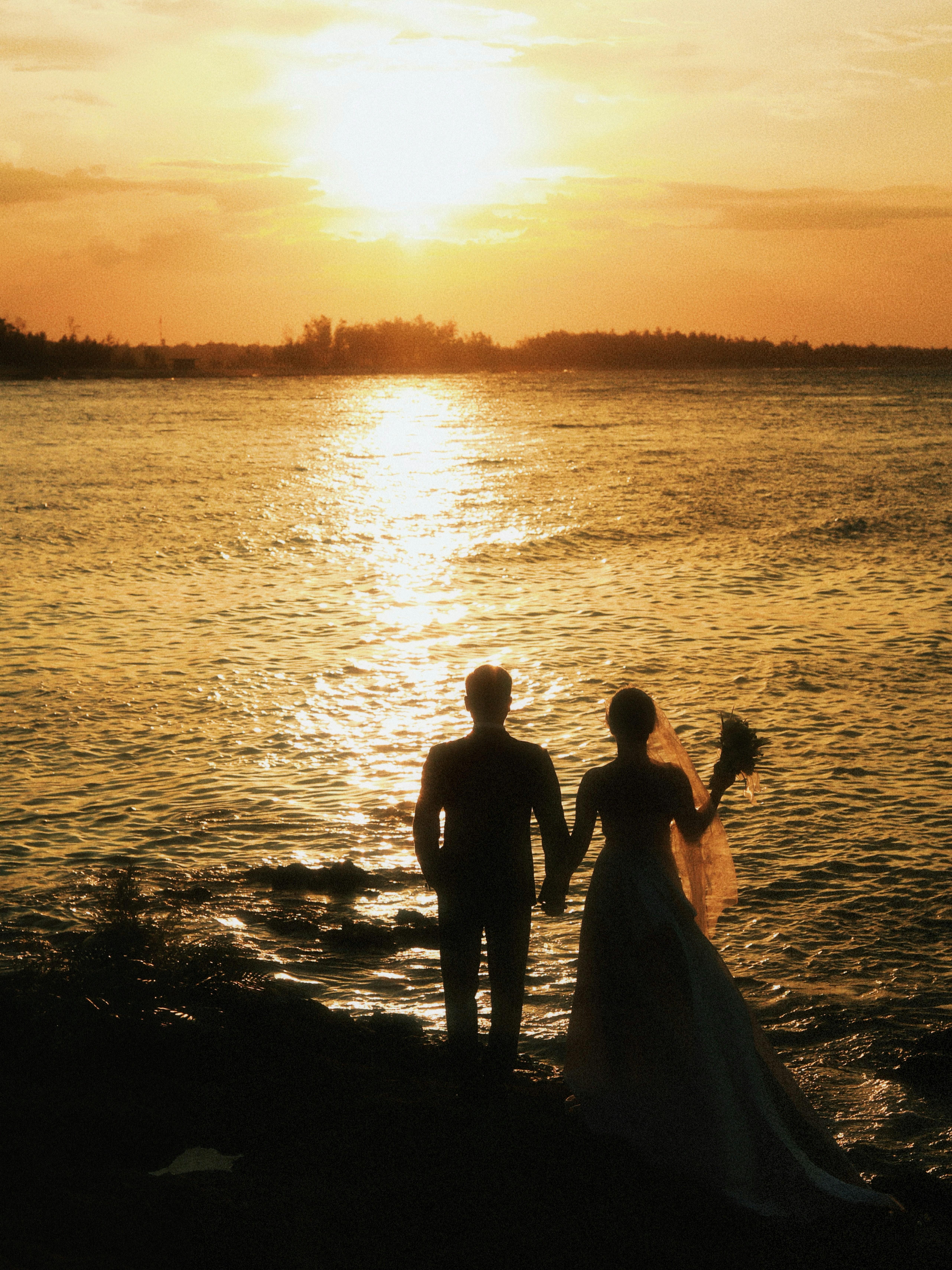 A couple holding hands watches the sunset over the ocean.