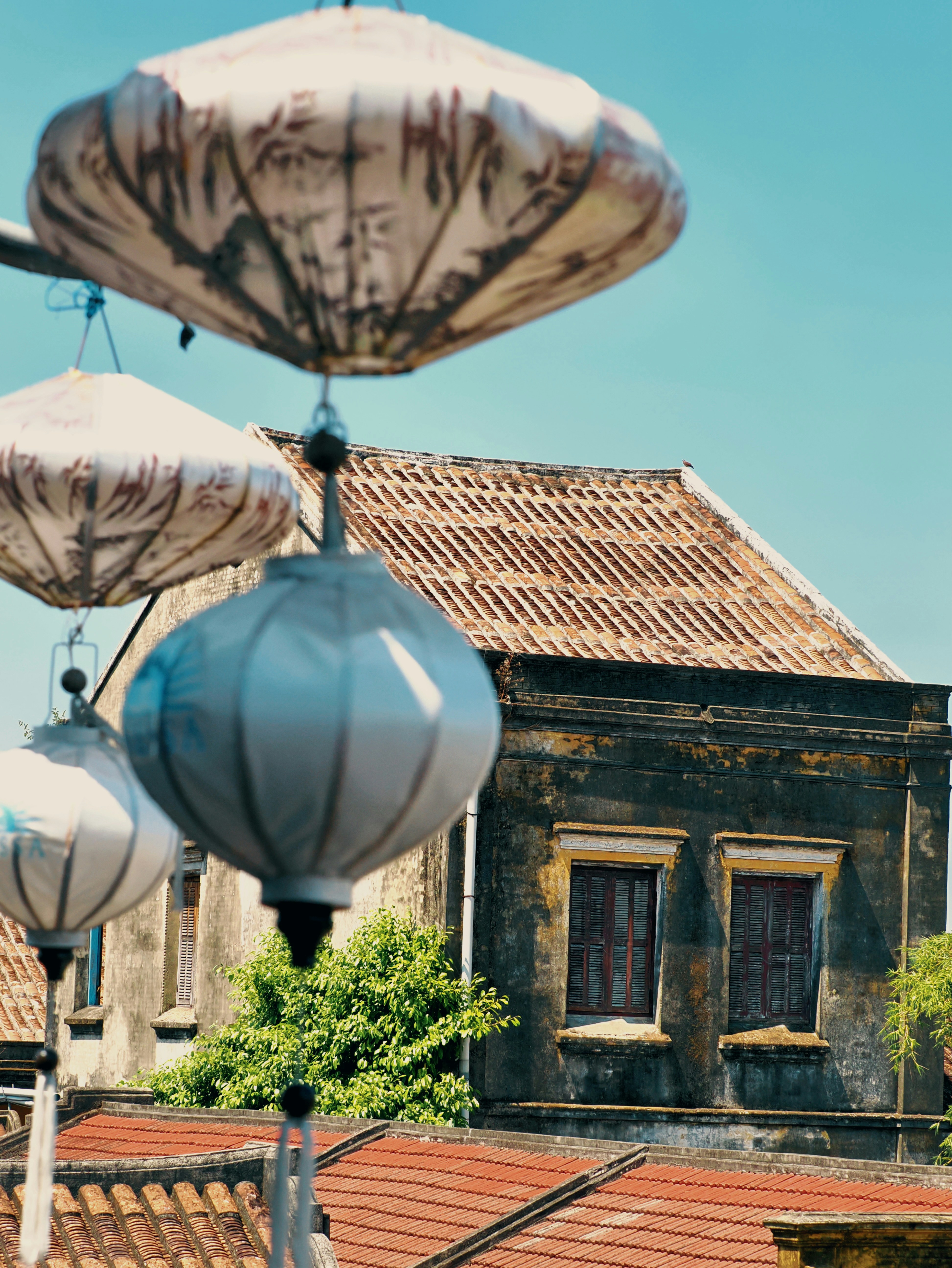 Traditional lanterns hang above old buildings under a blue sky.