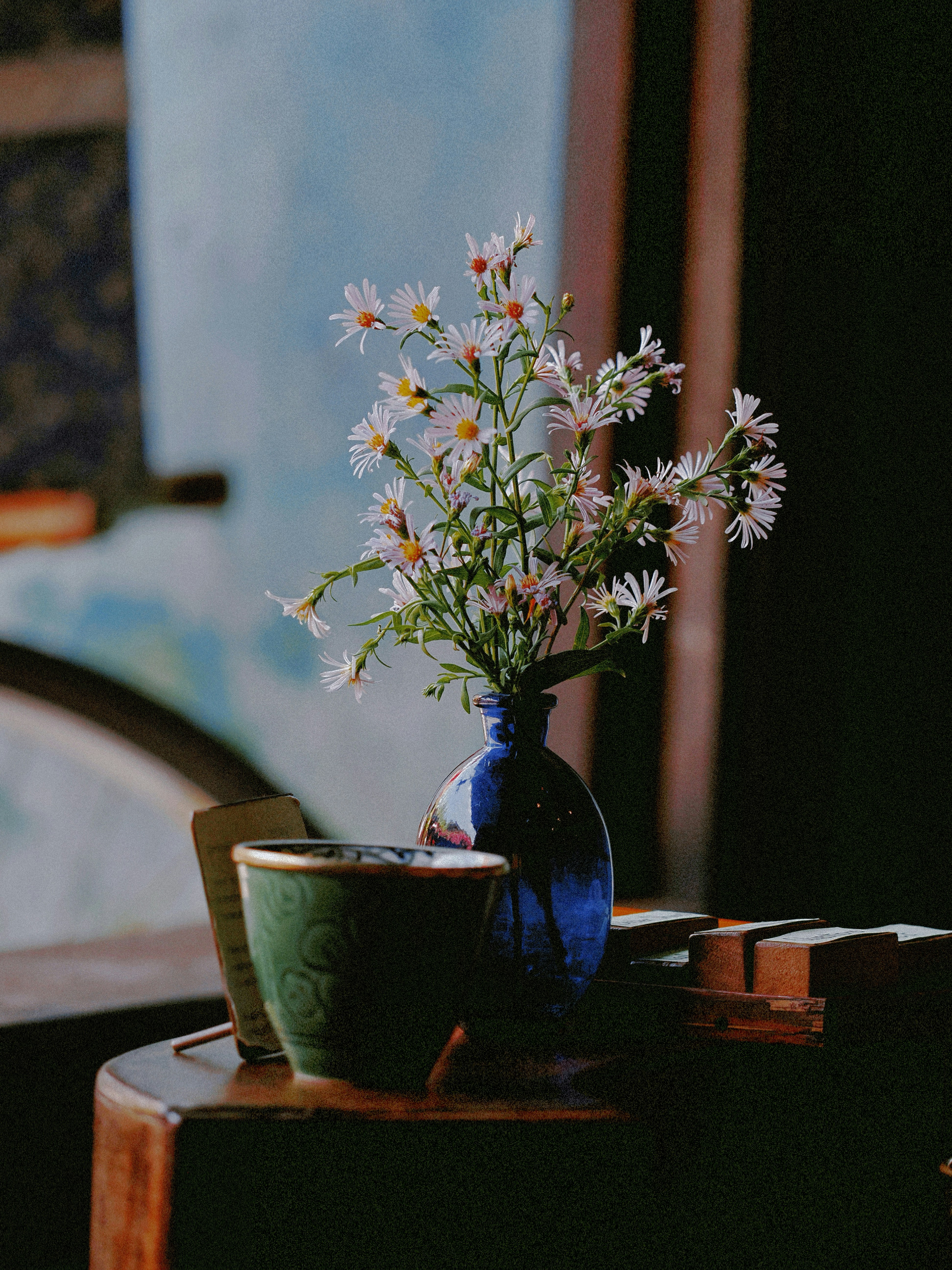 White flowers in a blue vase with a green cup.