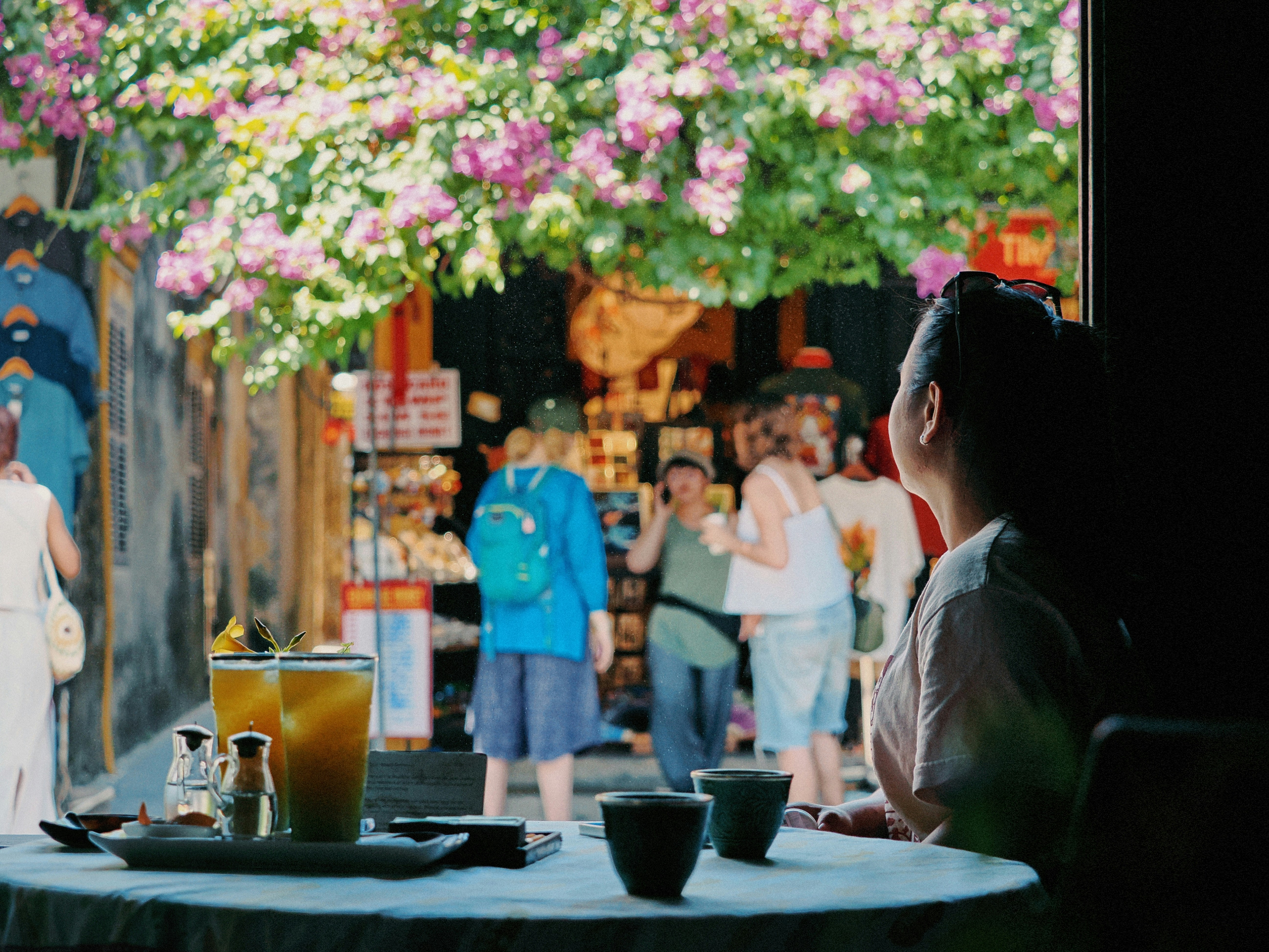 Person at table with drinks looks at lively street scene.