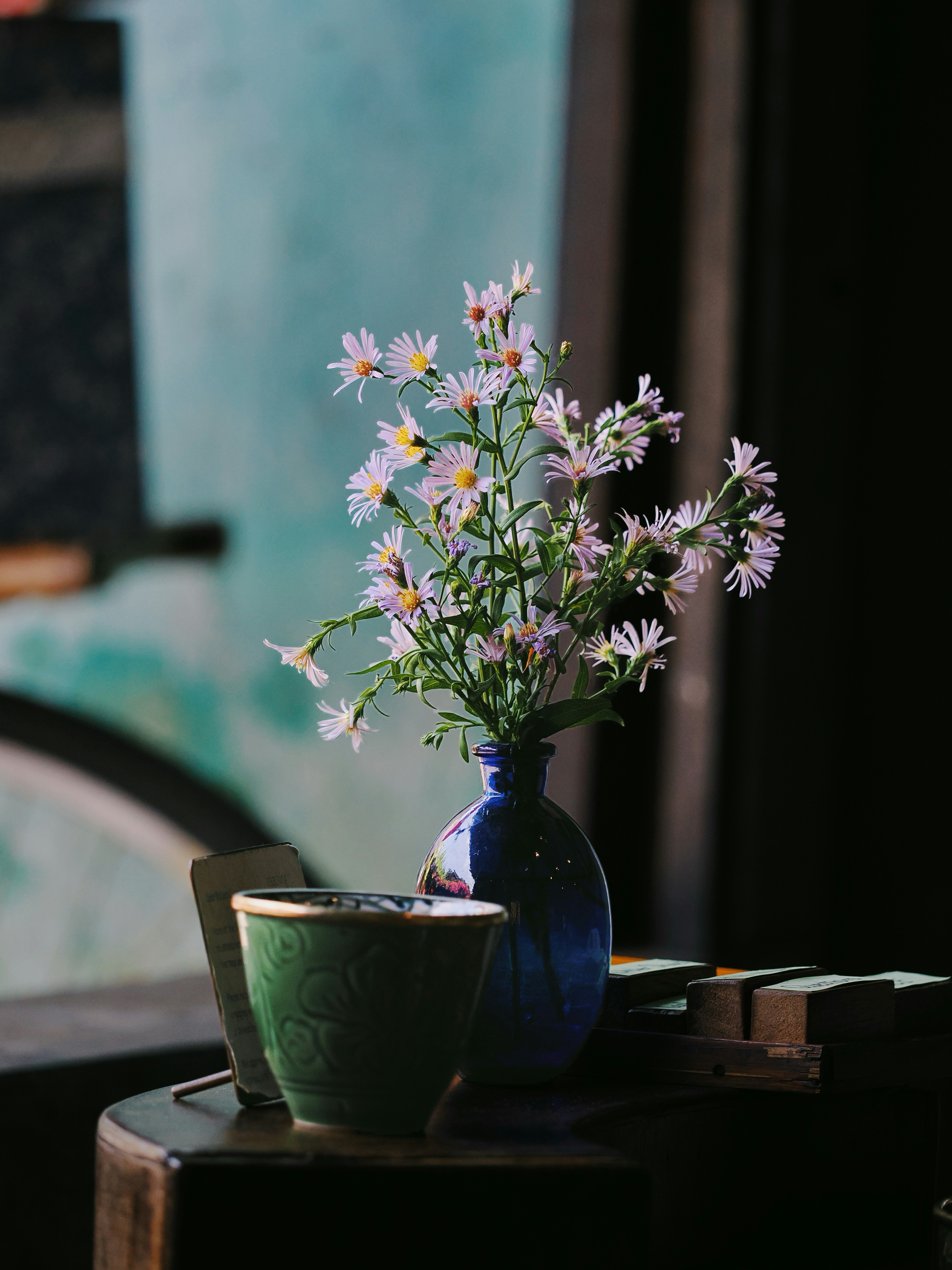 White flowers in blue vase beside a green cup.