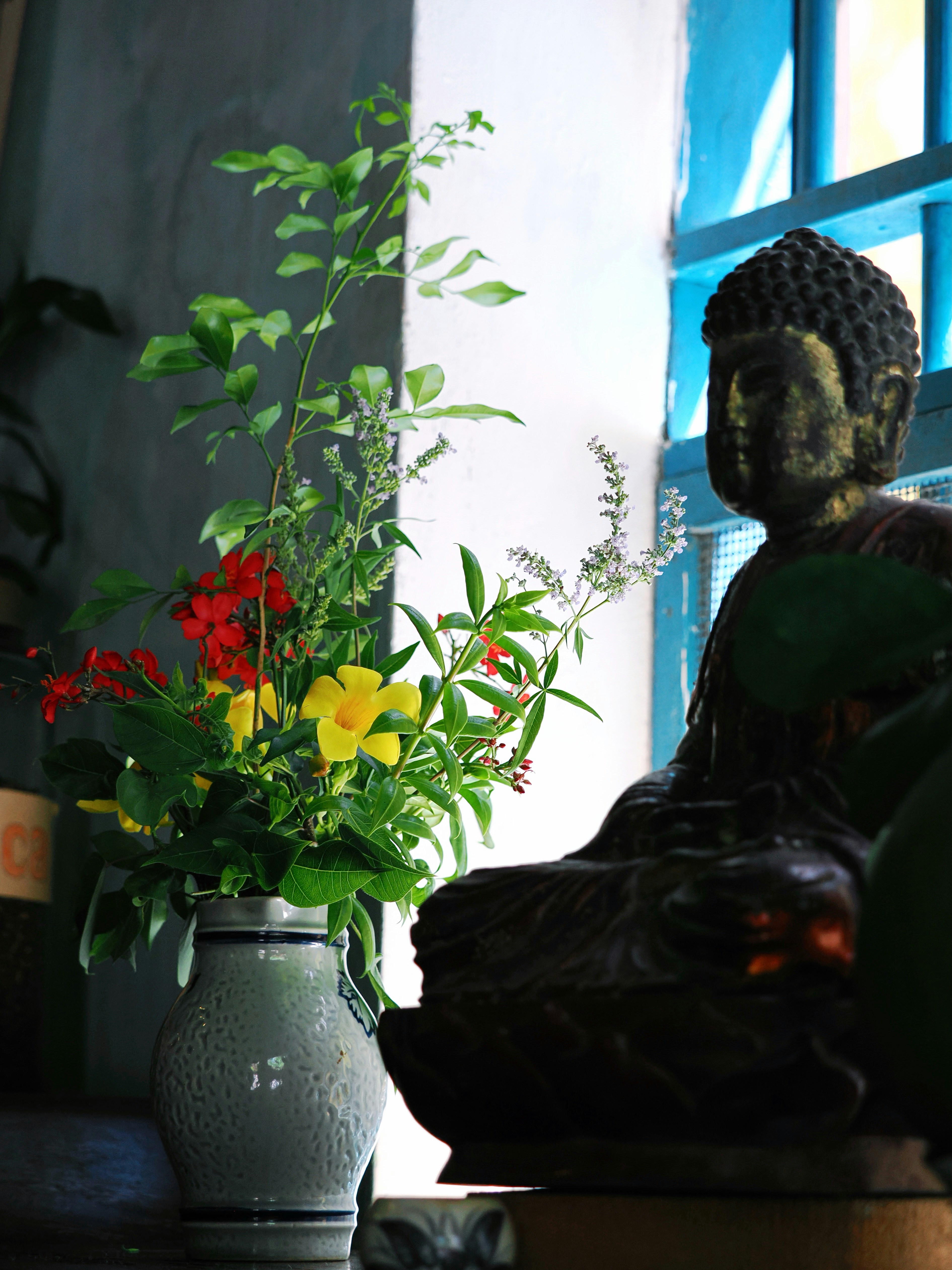 Buddha statue and vase of colorful flowers indoors.