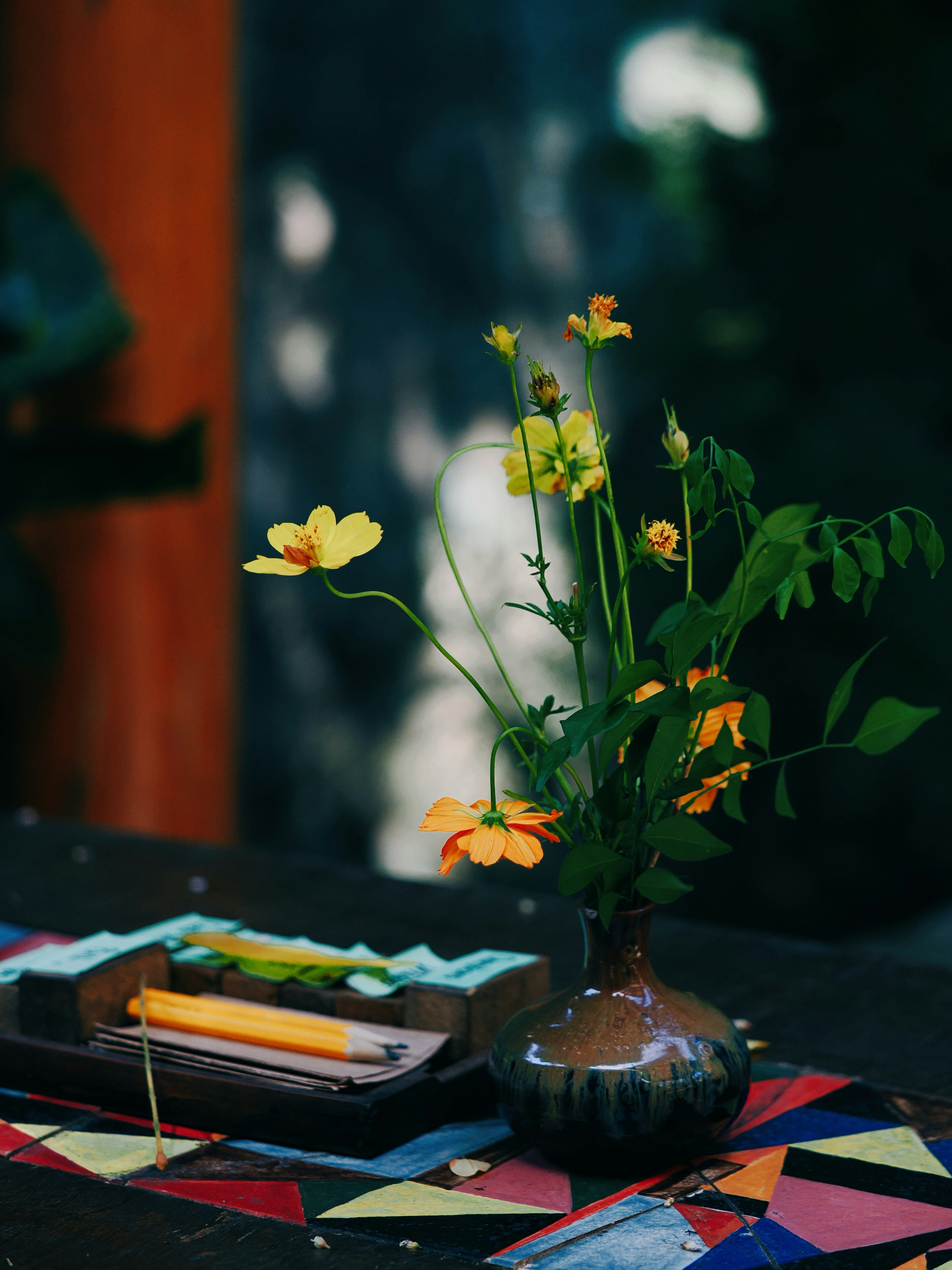 Yellow flowers in a vase on a table with pencils.