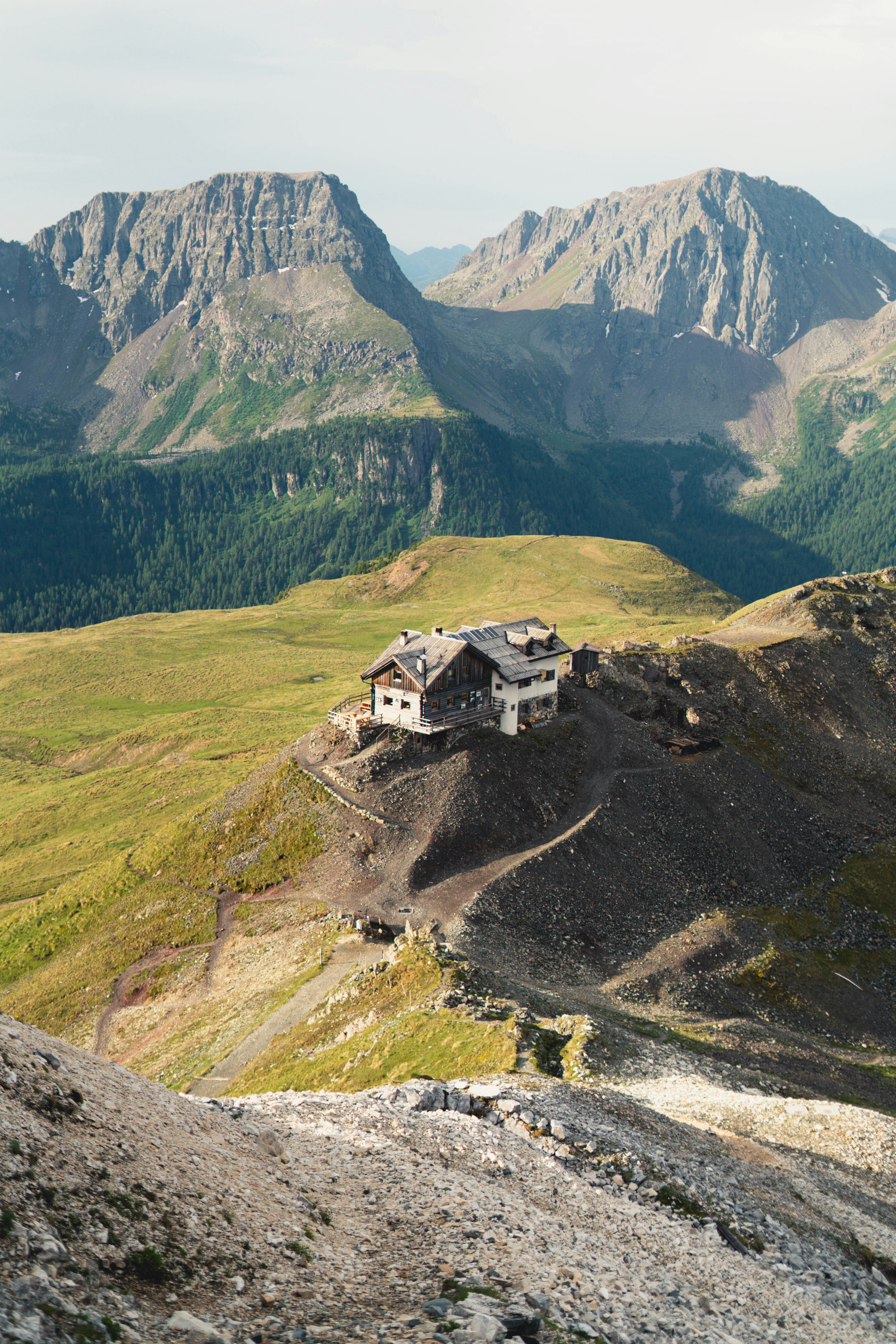 Alpine hut on a rocky mountain ridge with distant peaks.