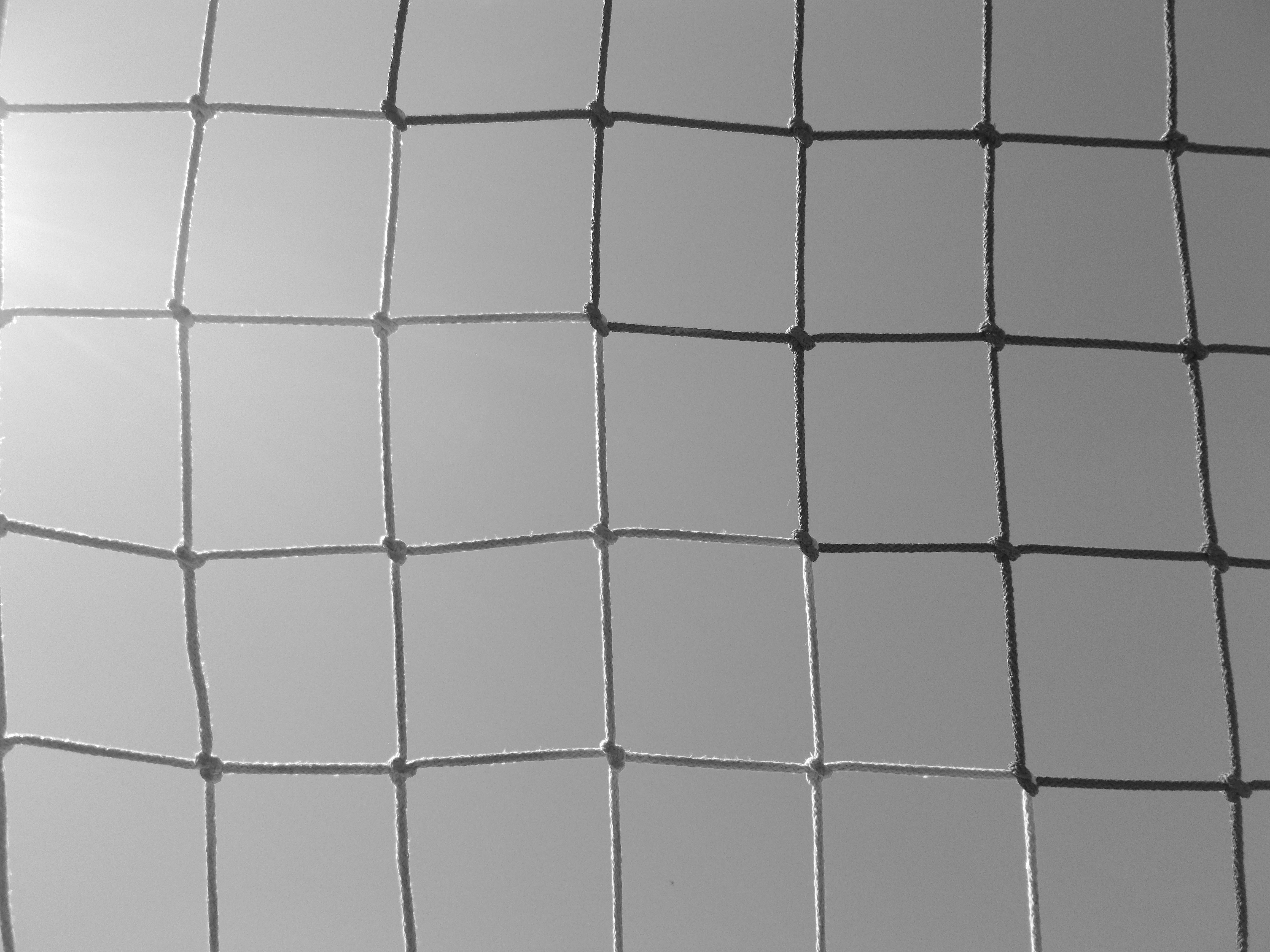 Monochrome grid of square panels basking in sunlight with softened edges and slight perspective, revealing a repetitive mesh structure.
