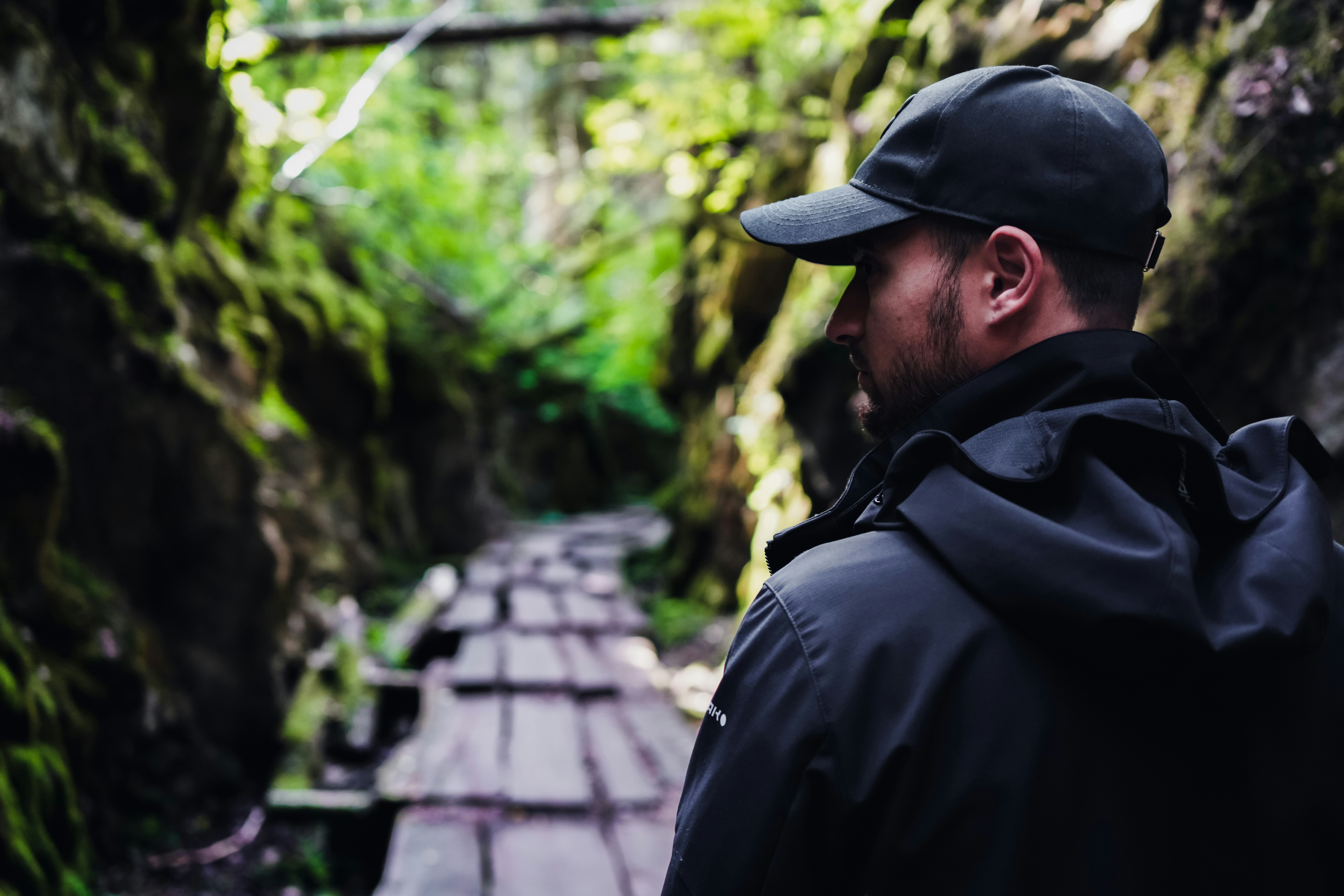 Hiker on a wooden boardwalk in a narrow, moss-covered gorge.