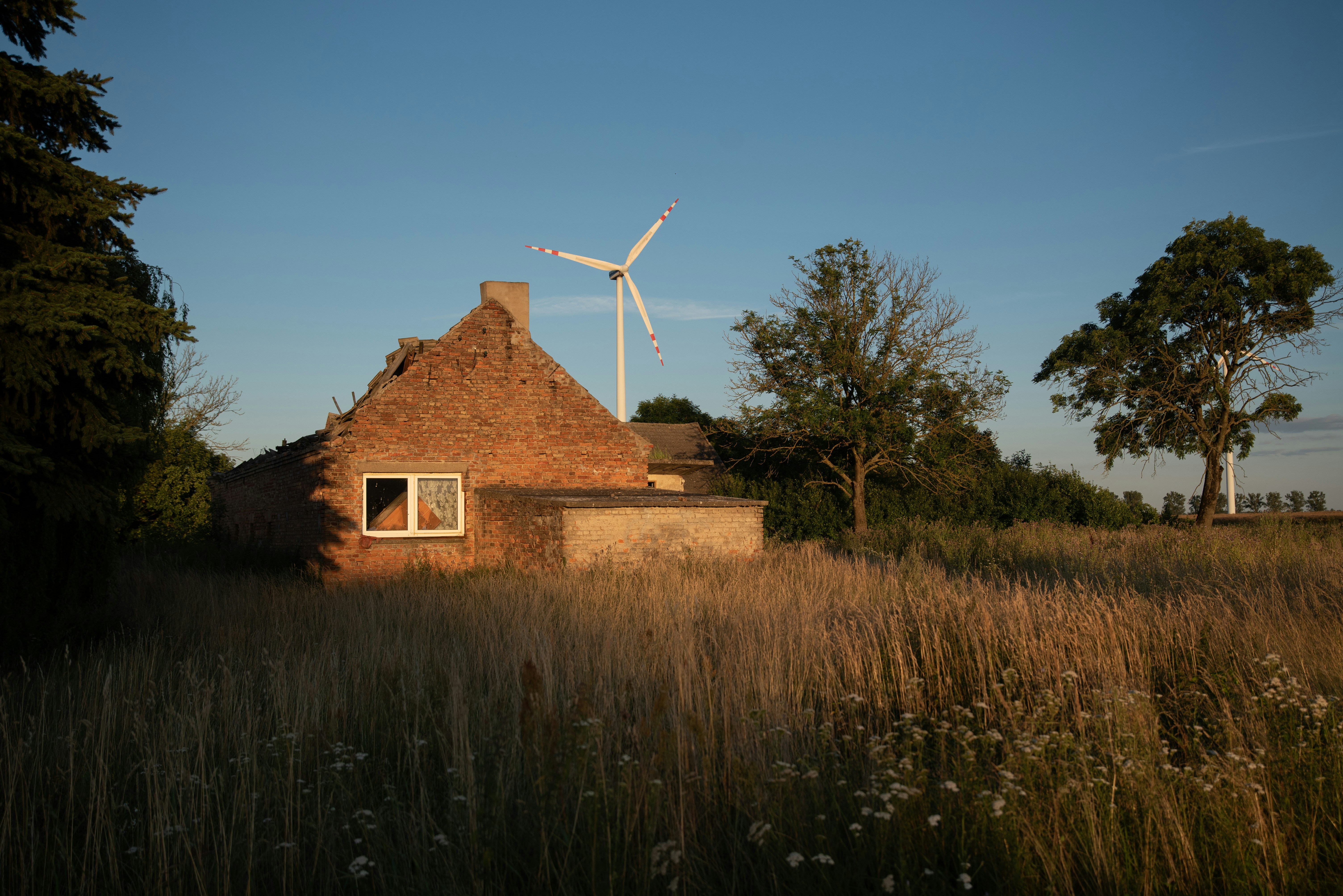 Old brick house, wind turbine, and dry field at sunset
