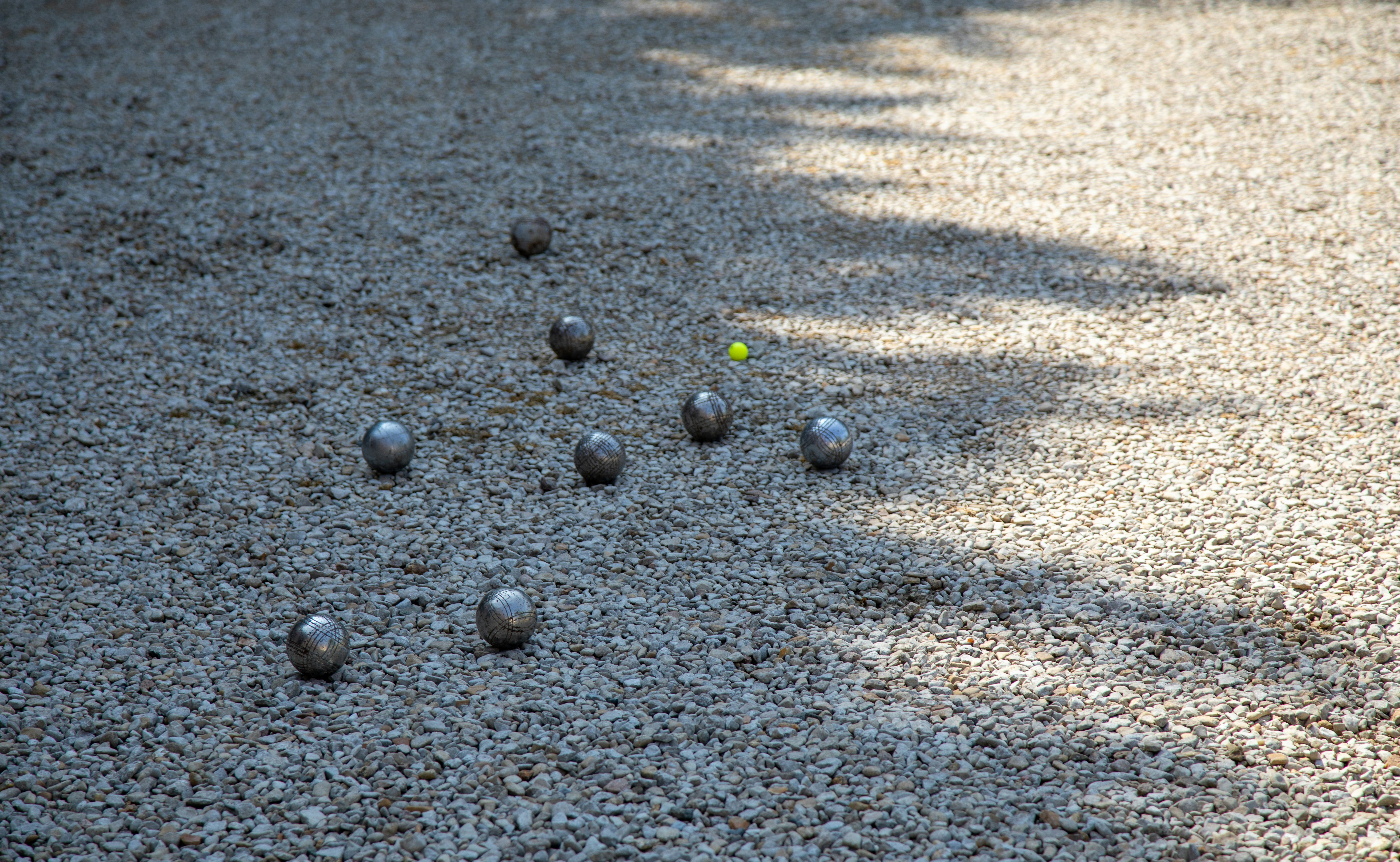 Metallic boules and a yellow target ball on gravel.