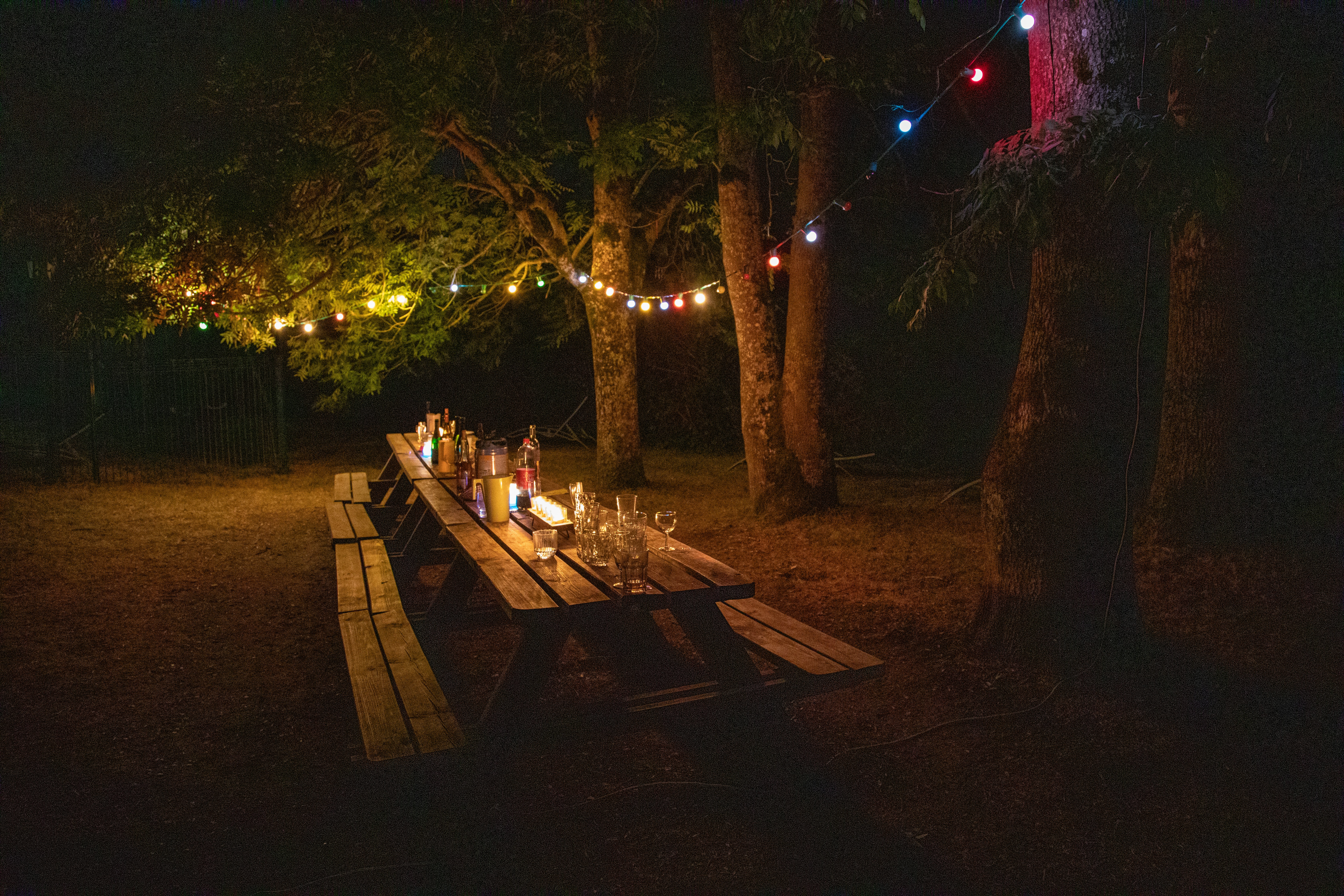 Outdoor picnic table illuminated by colorful string lights at night.