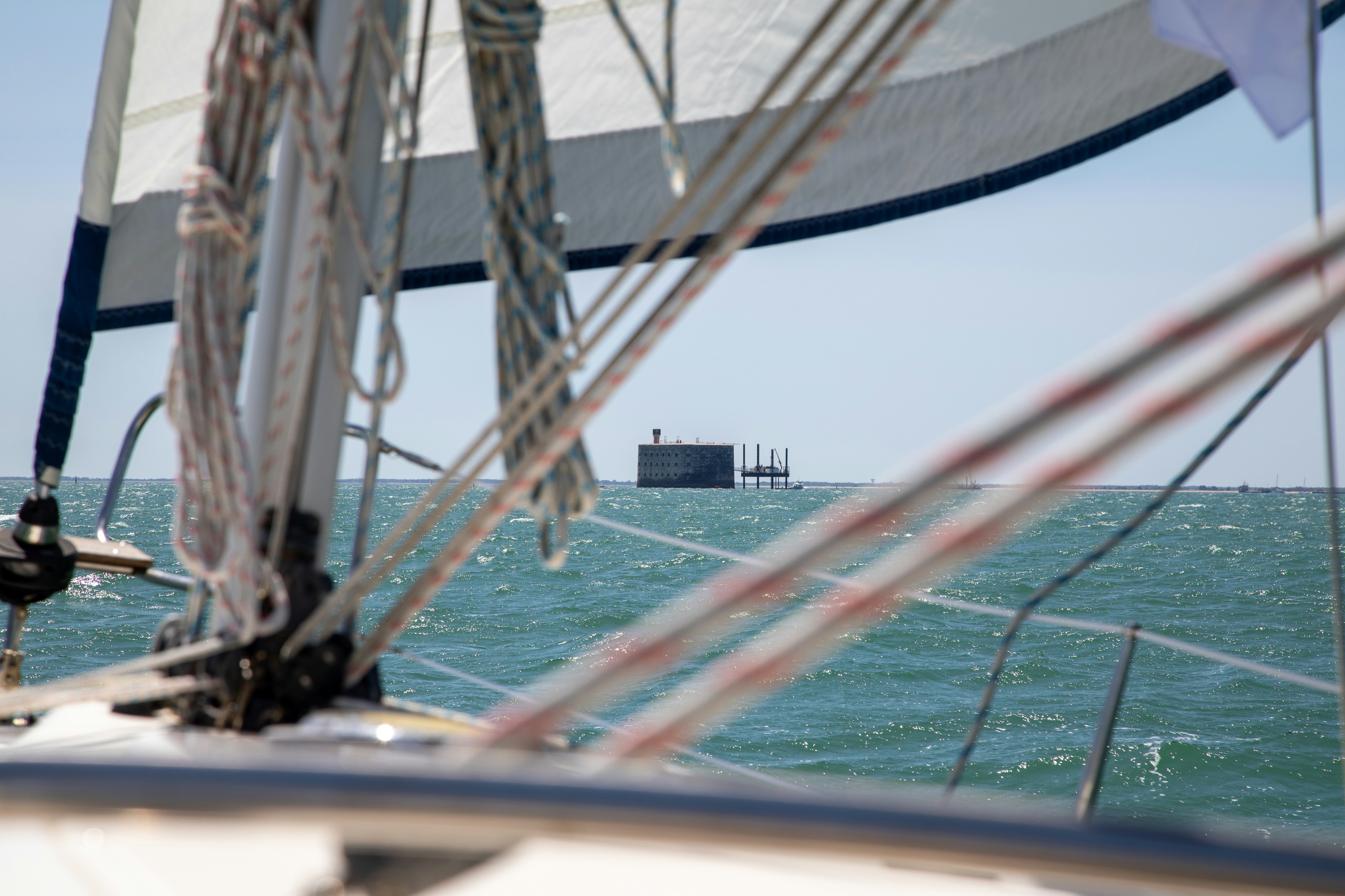 Distant sea fort viewed from a sailboat's rigging.
