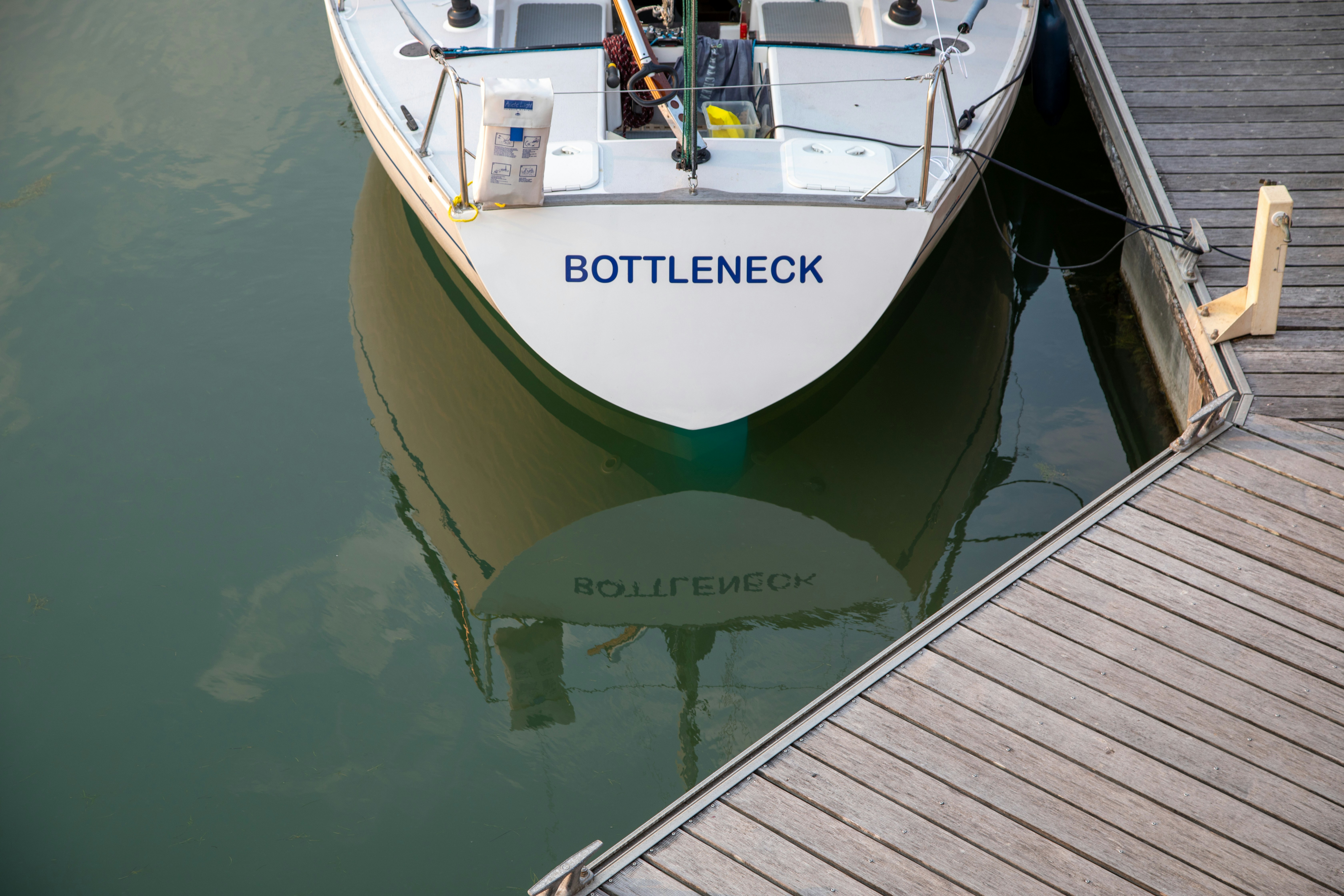 White sailboat "bottleneck" docked beside a wooden pier.