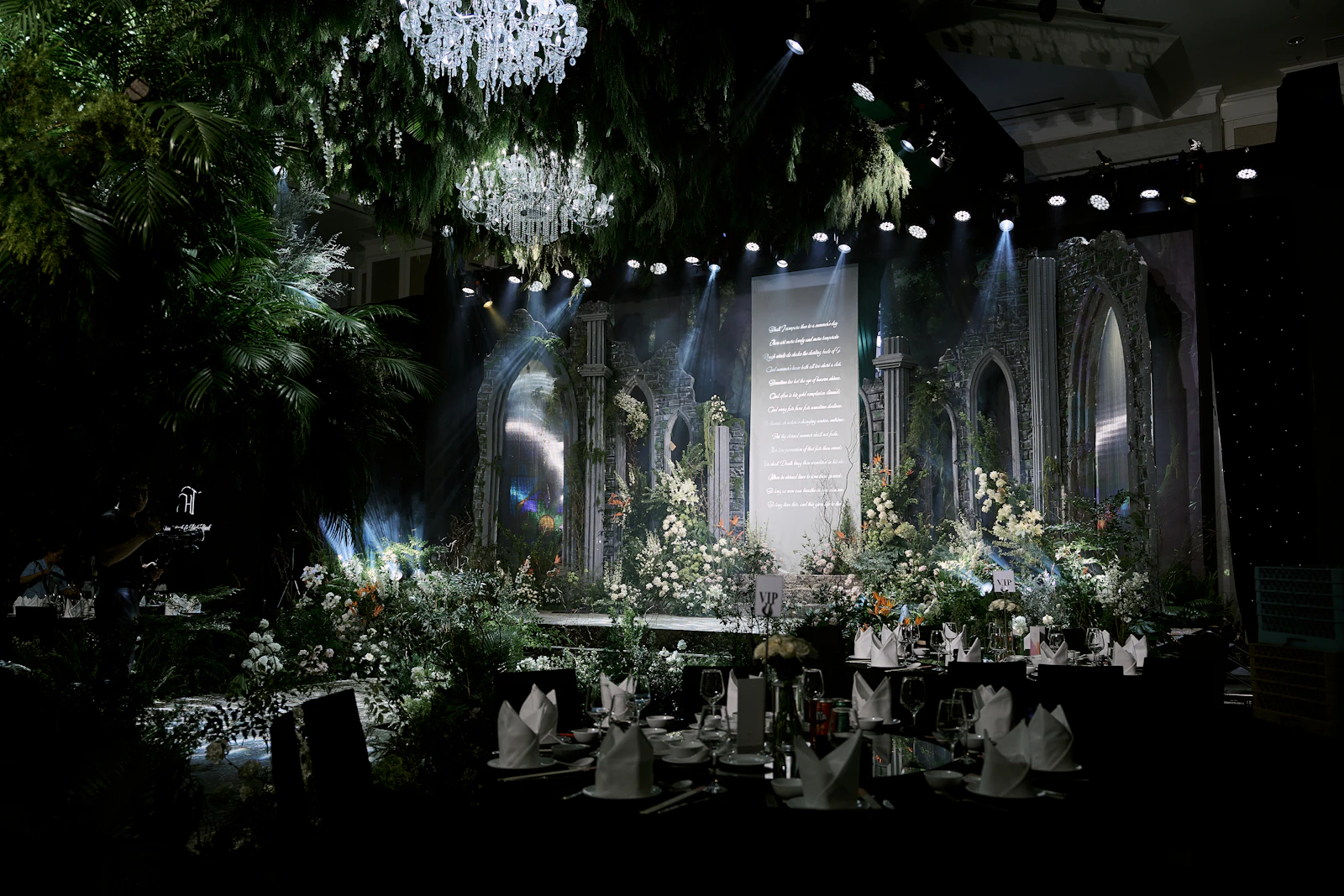 An event stage dressed with white flowers under chandeliers