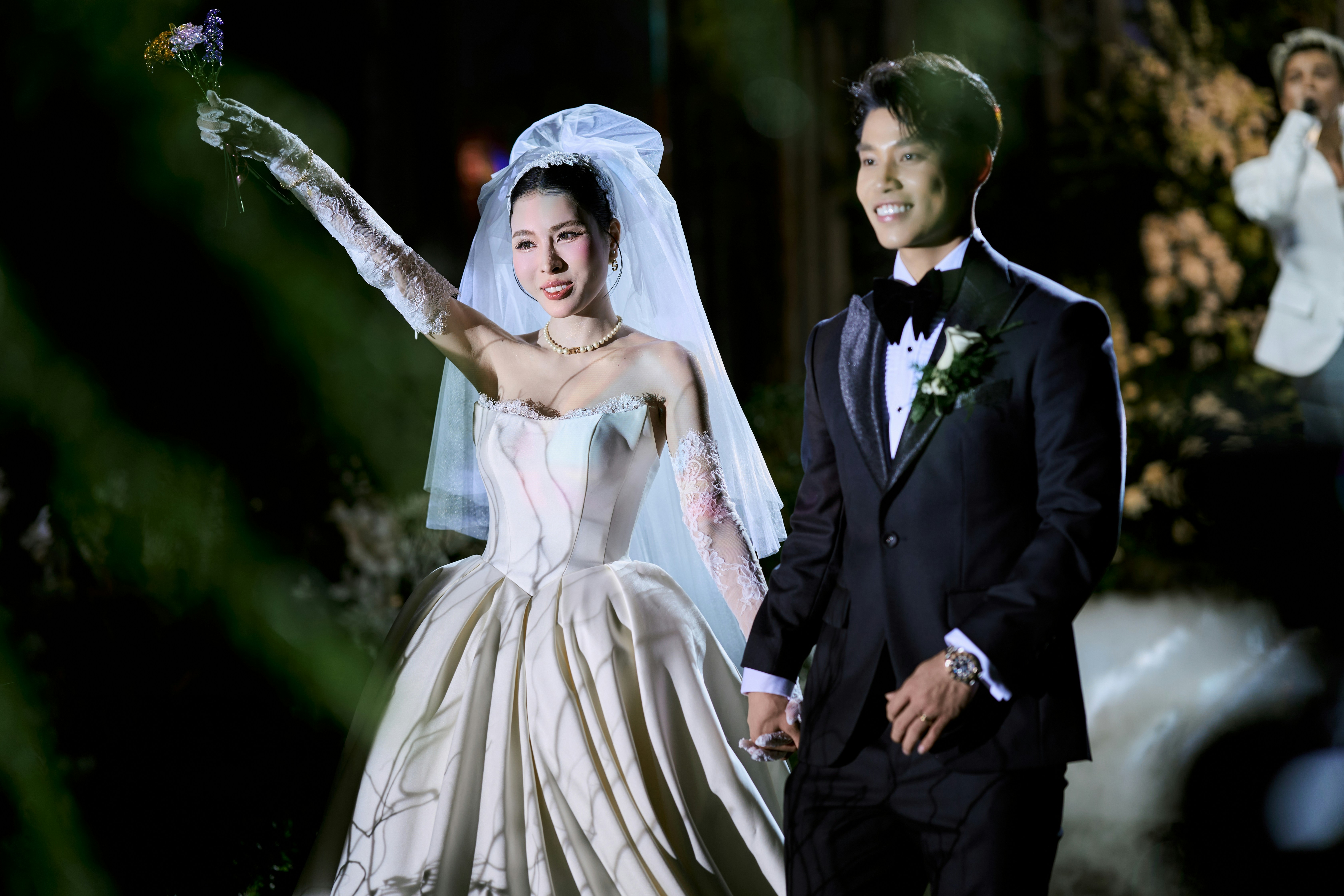 Bride raises bouquet while groom smiles at their wedding