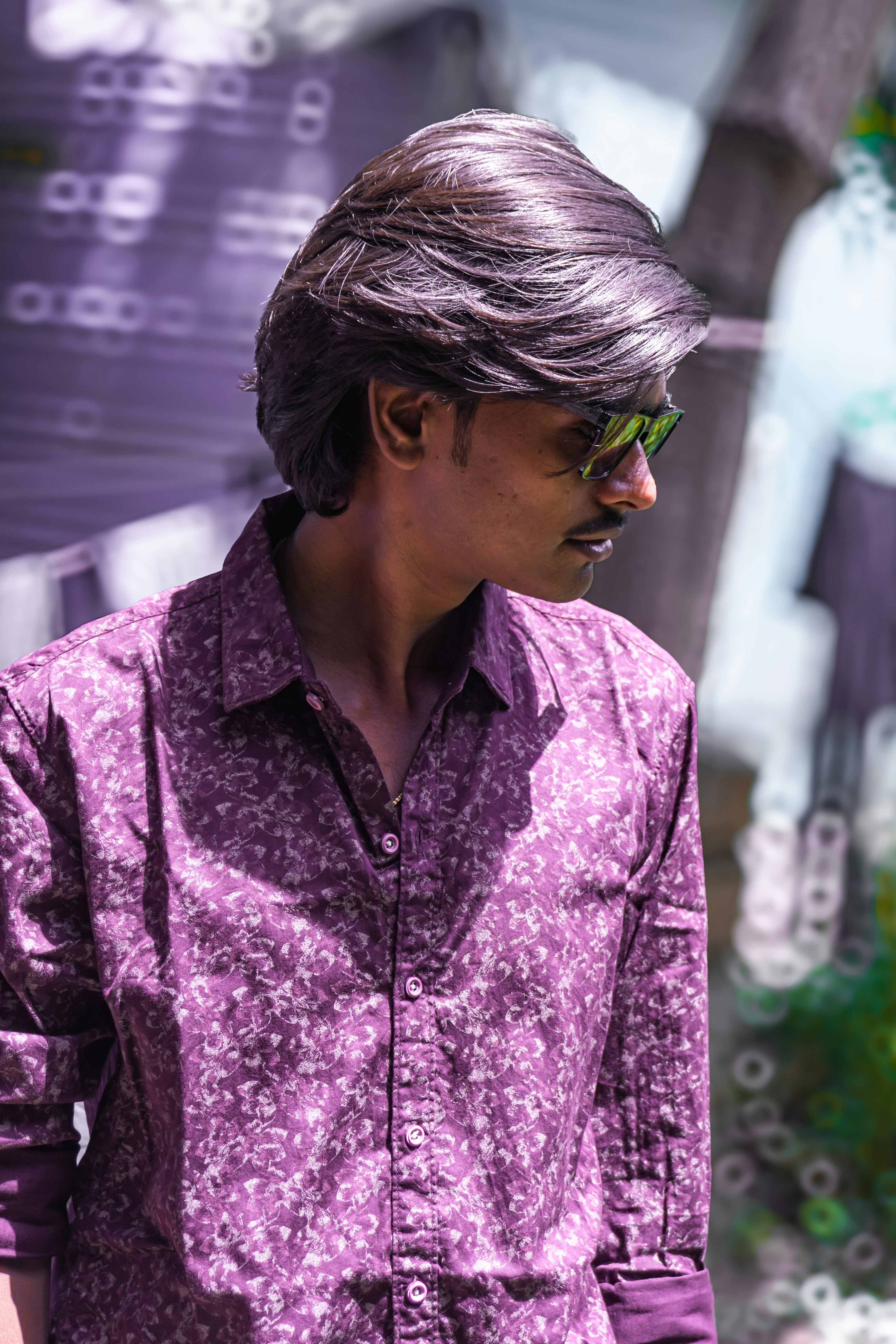 Jeune homme en chemise à motifs violets et lunettes de soleil.