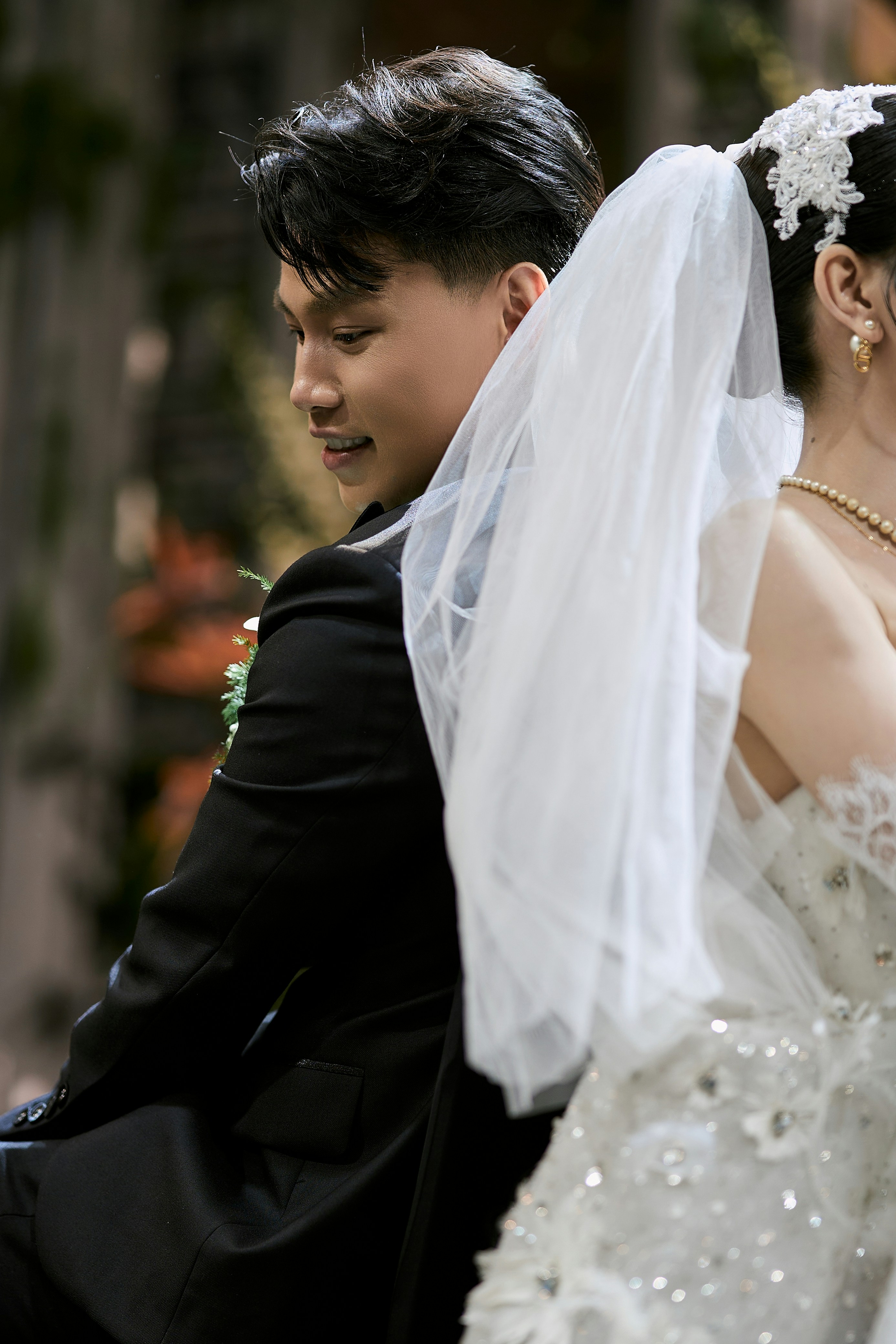 A smiling groom stands back-to-back with his veiled bride
