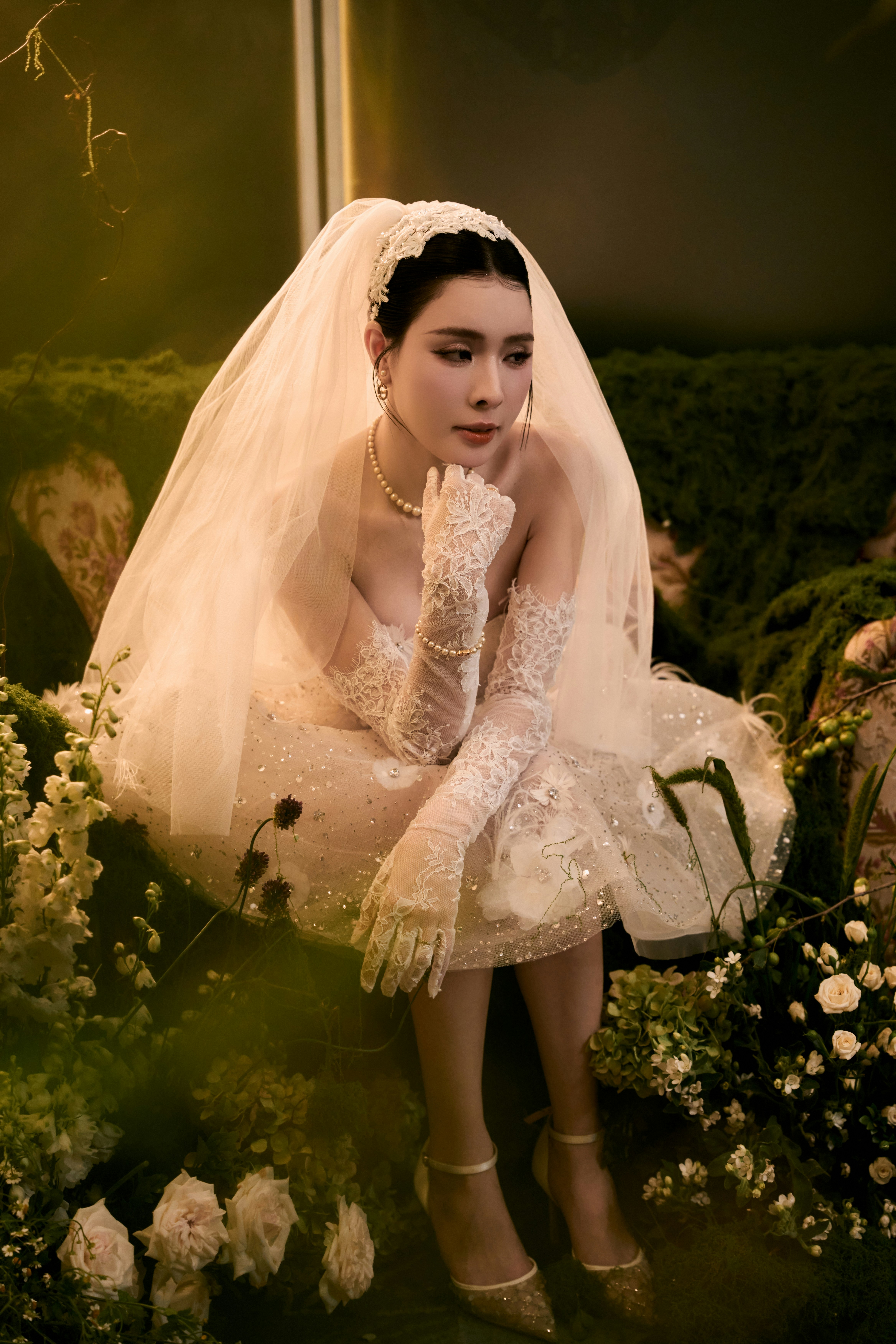 Pensive bride in short gown and veil surrounded by flowers