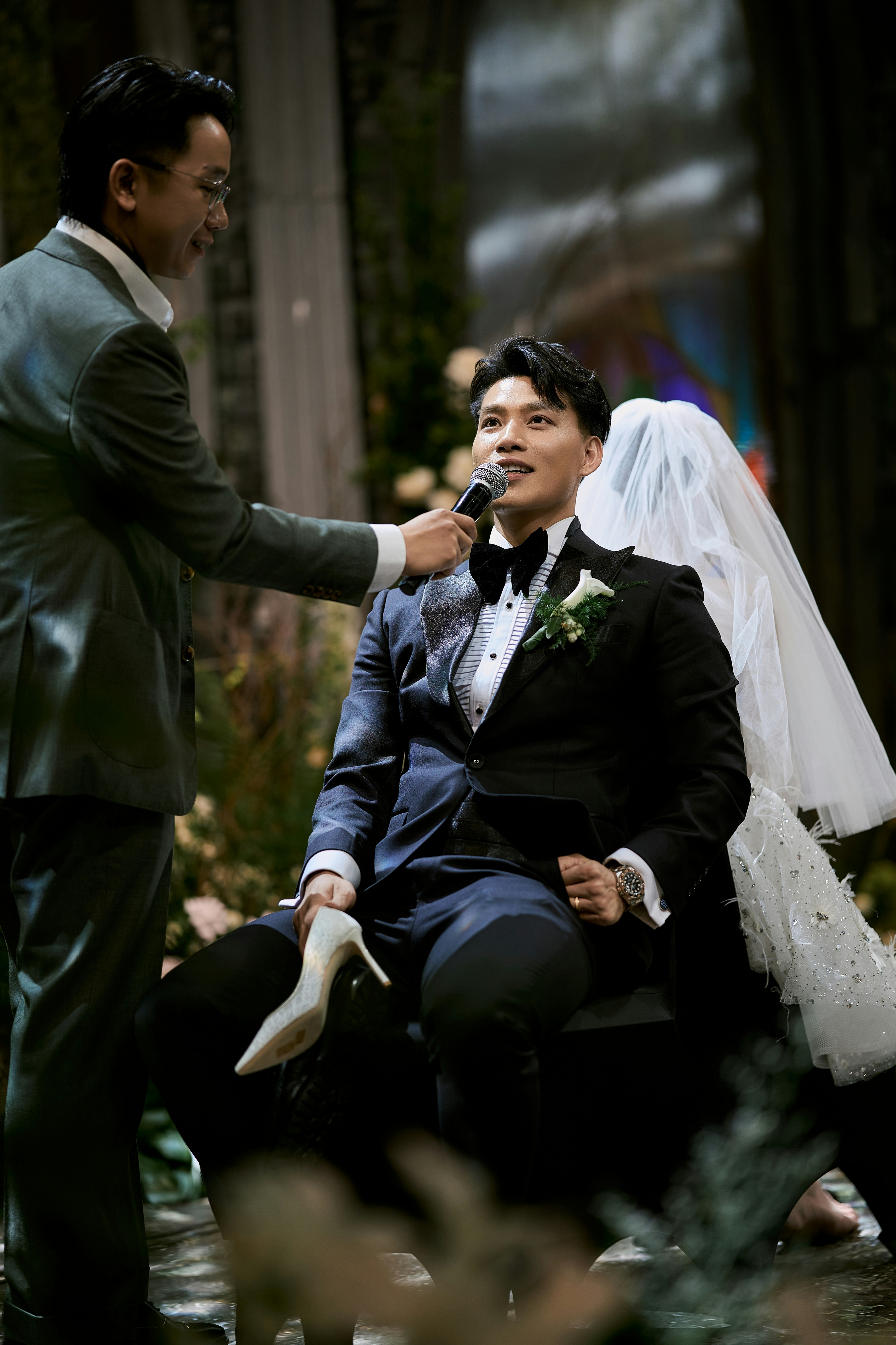 Groom holding a shoe and speaking into a microphone.