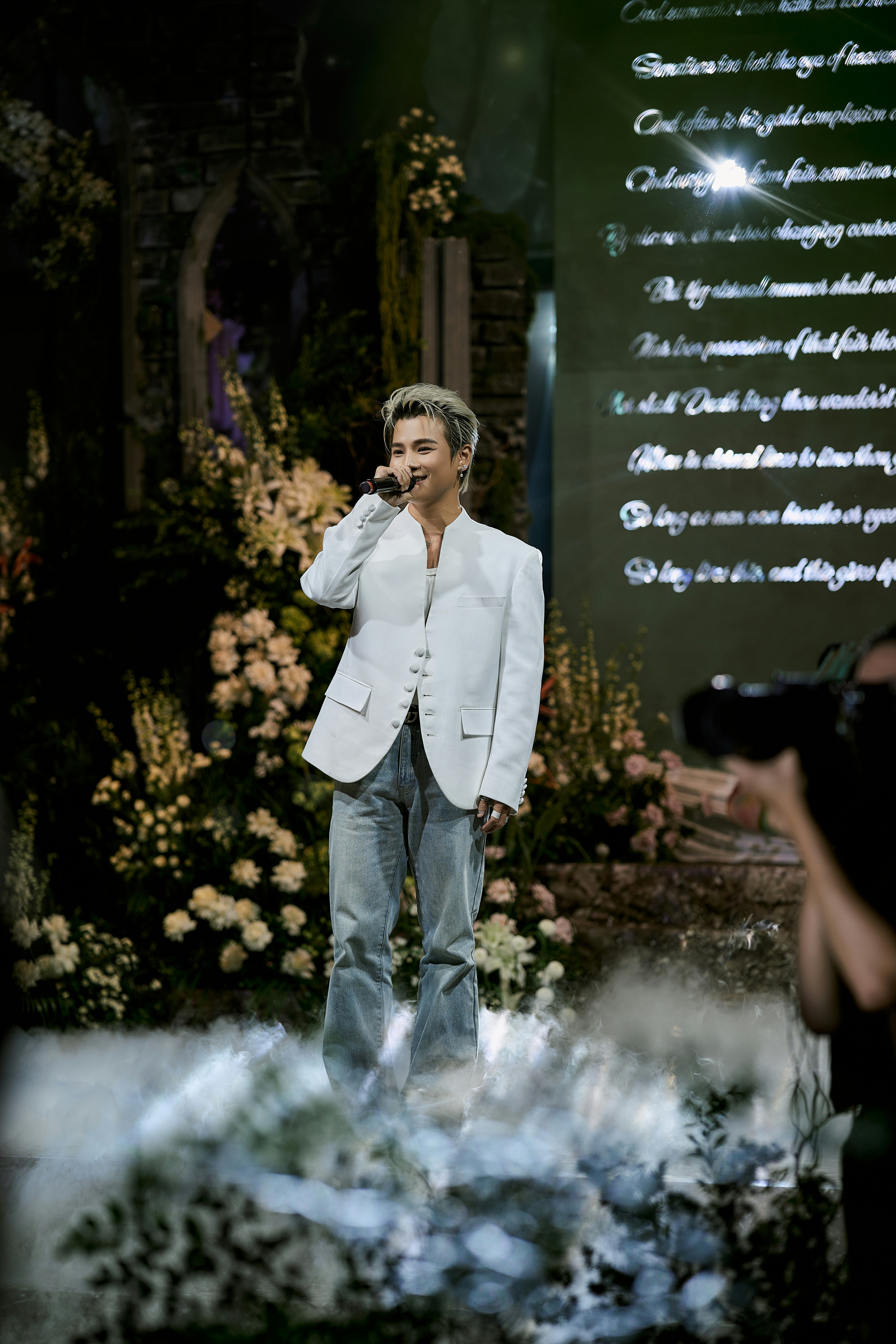 Man singing on stage surrounded by flowers and mist
