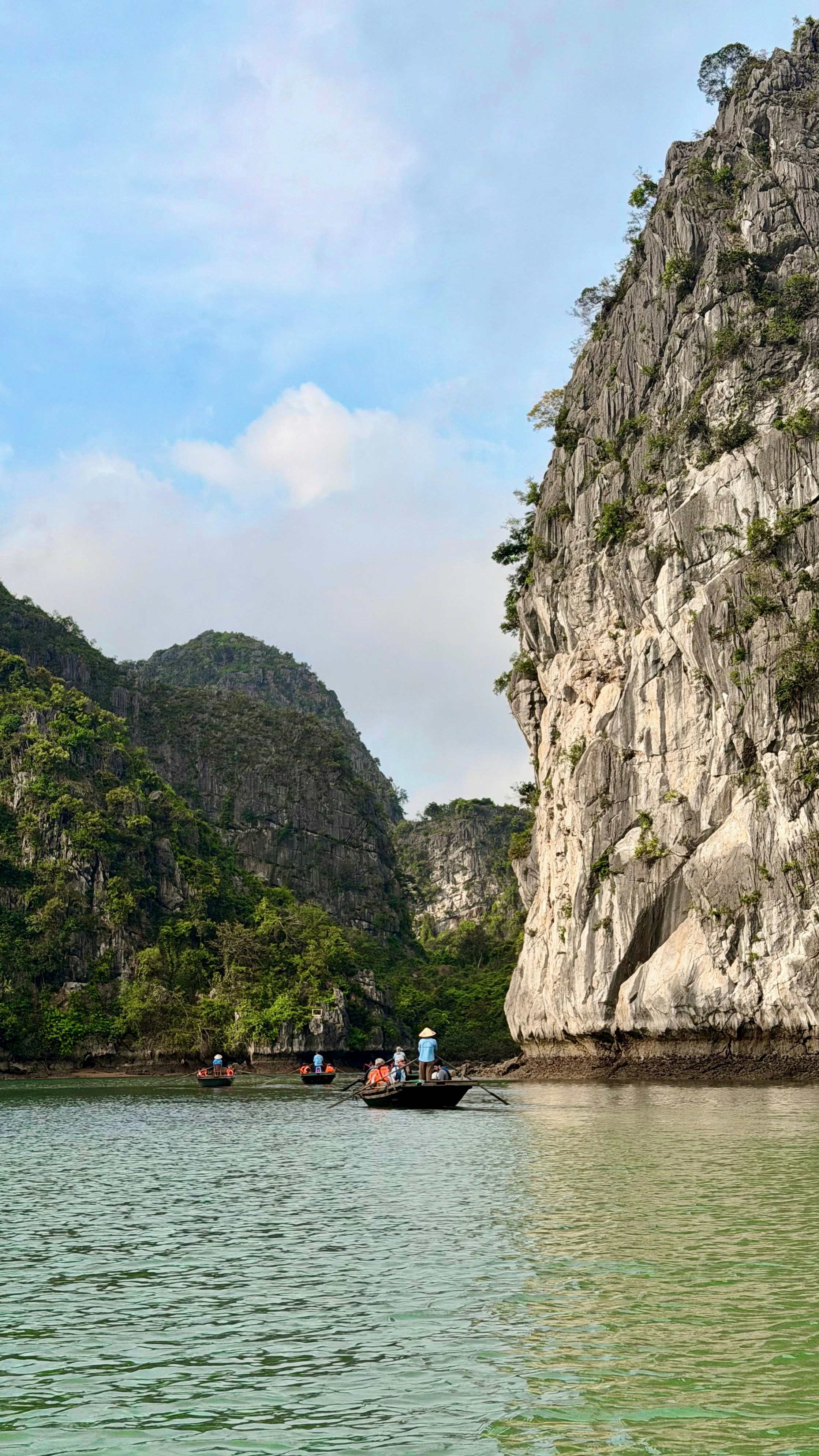 Small boats on green water surrounded by massive rocky cliffs.