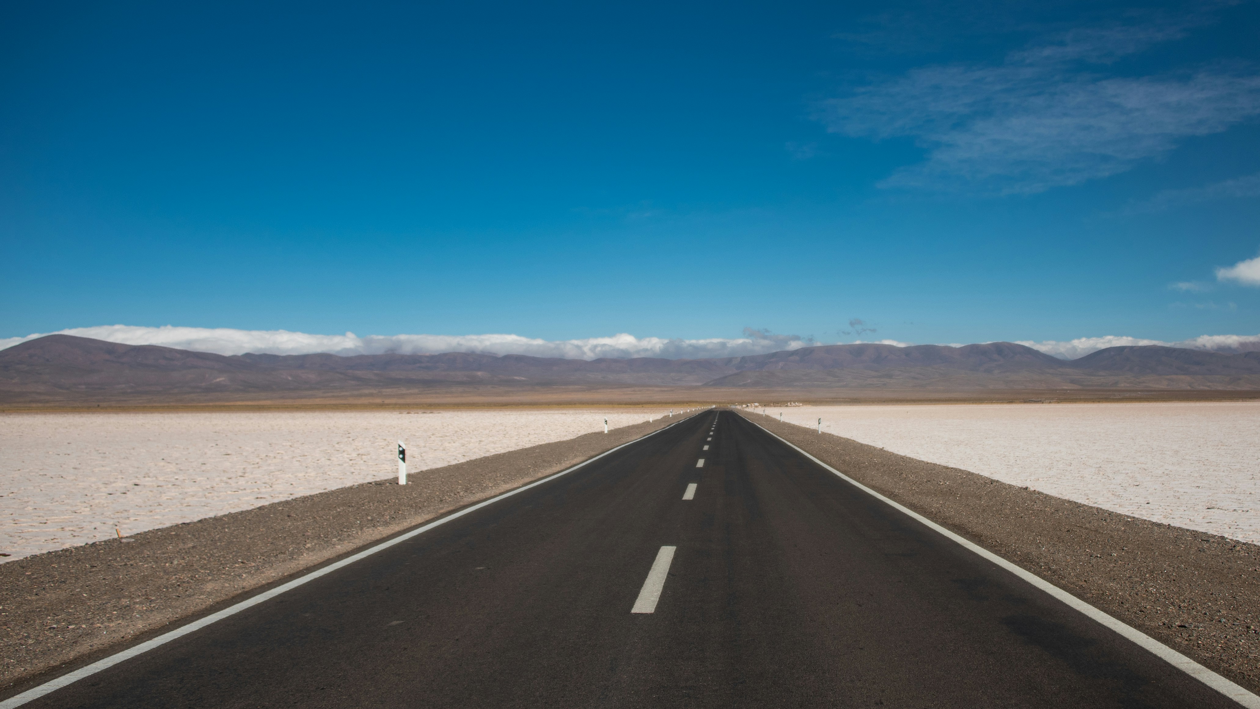 Endless road stretches across a salt flat towards distant mountains.