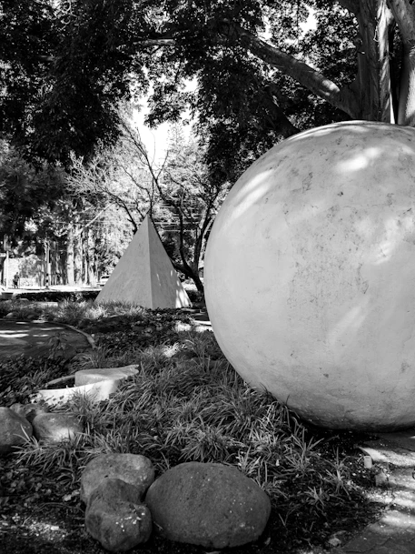Sculptural sphere and pyramid amidst trees in monochrome