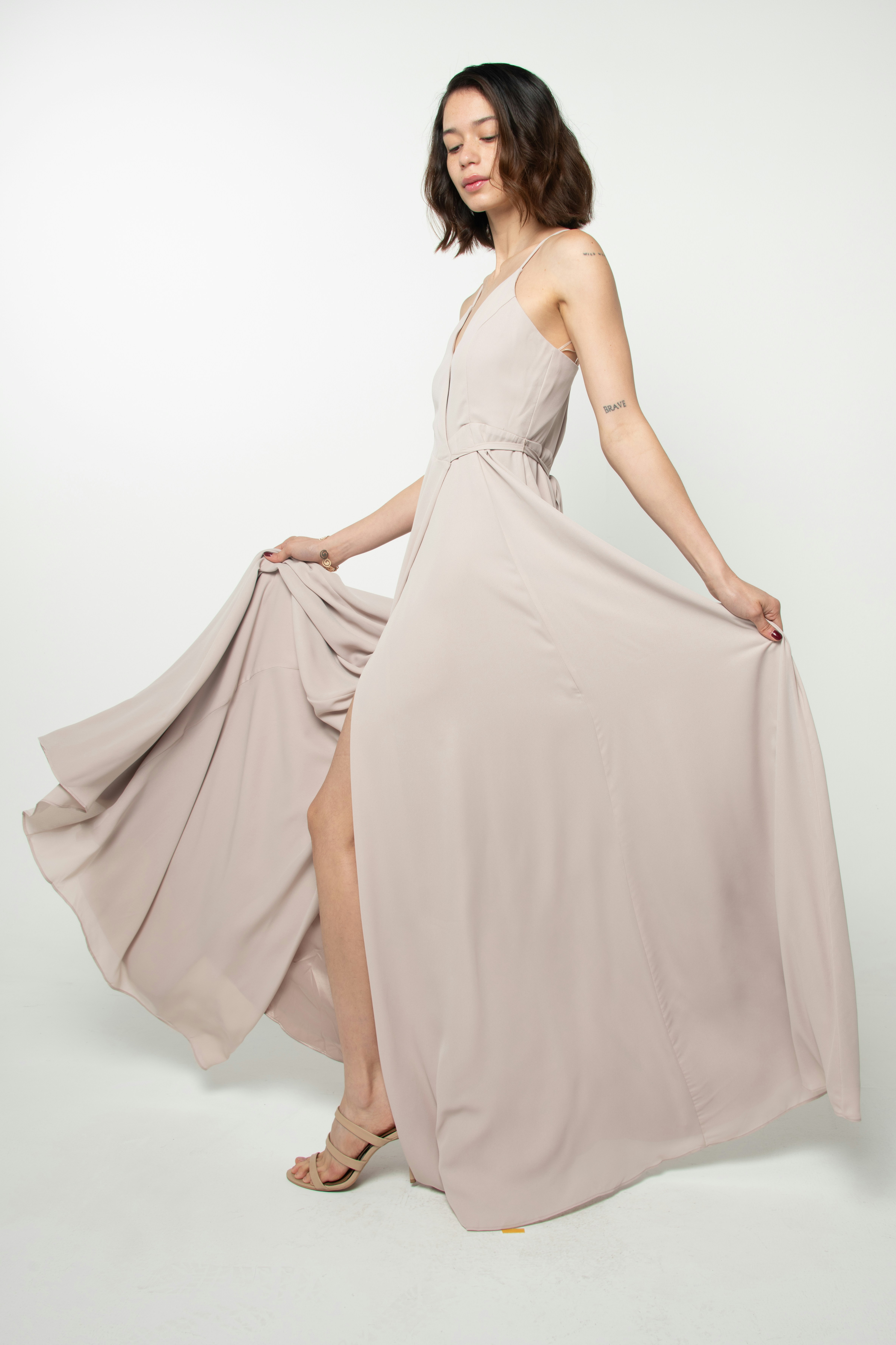 Modelo con vestido largo de tiras color rosa arena, sosteniendo la falda abierta