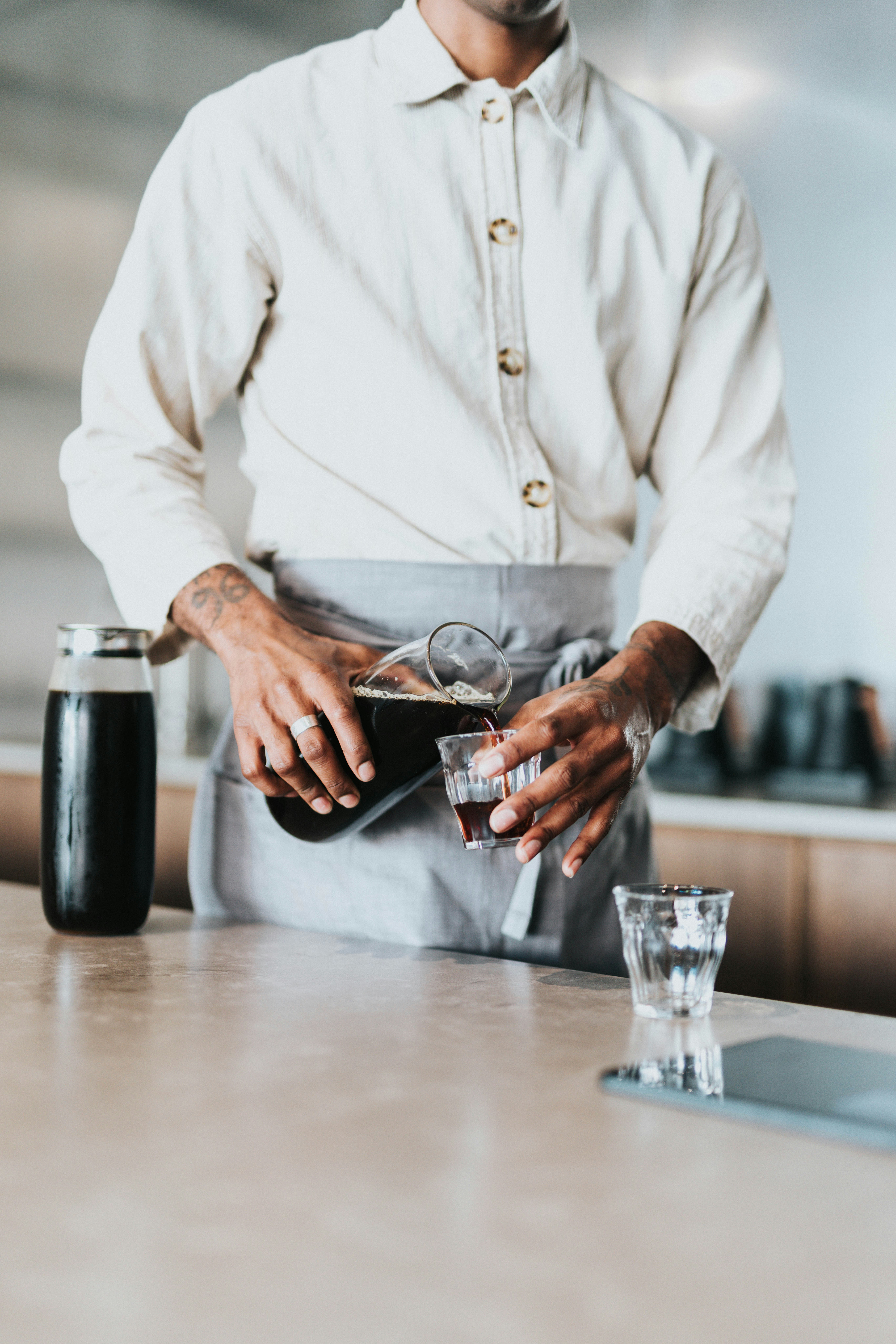 Person pouring dark liquid into a small glass.
