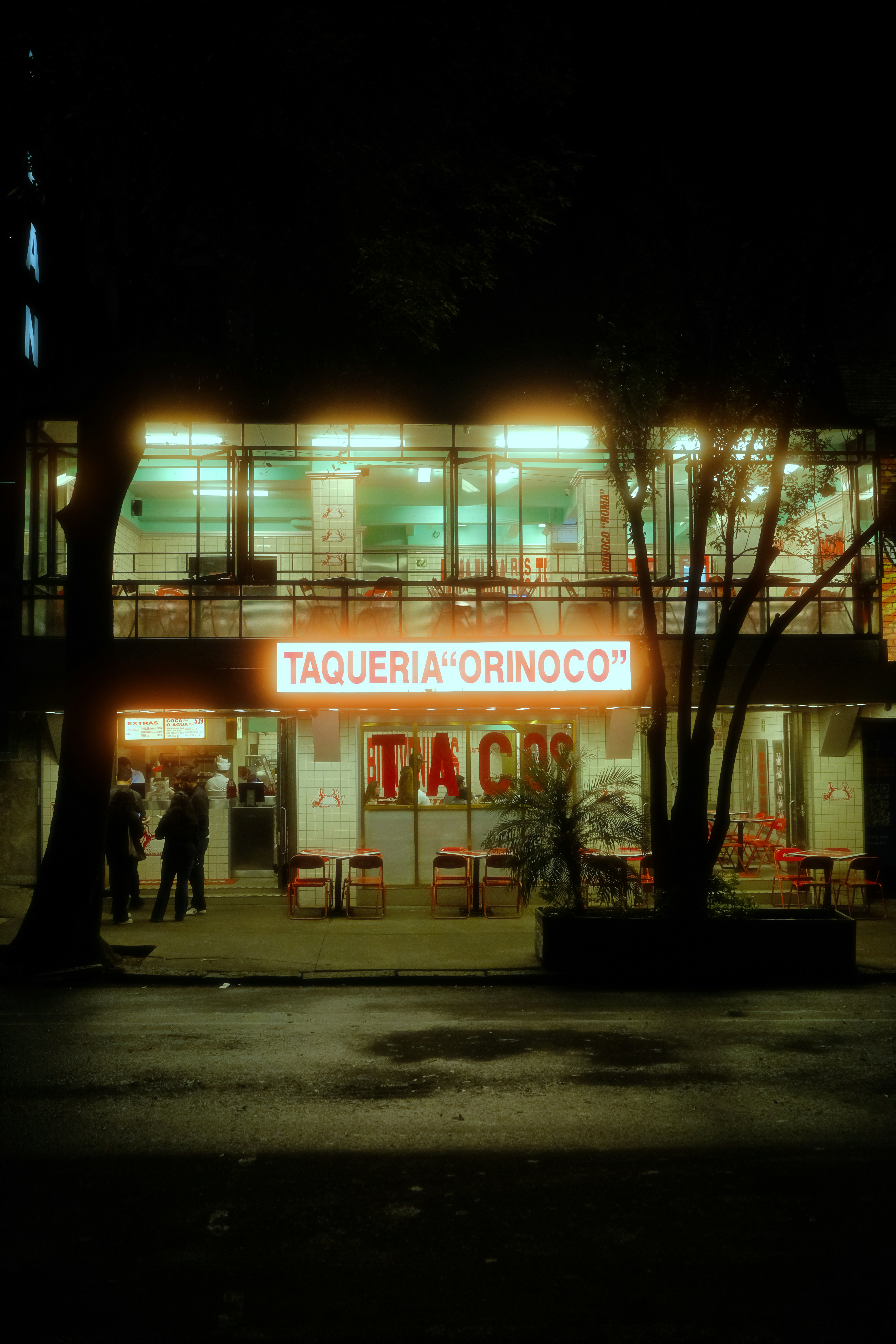 Neon-lit taqueria orinoco at night with people and reflections