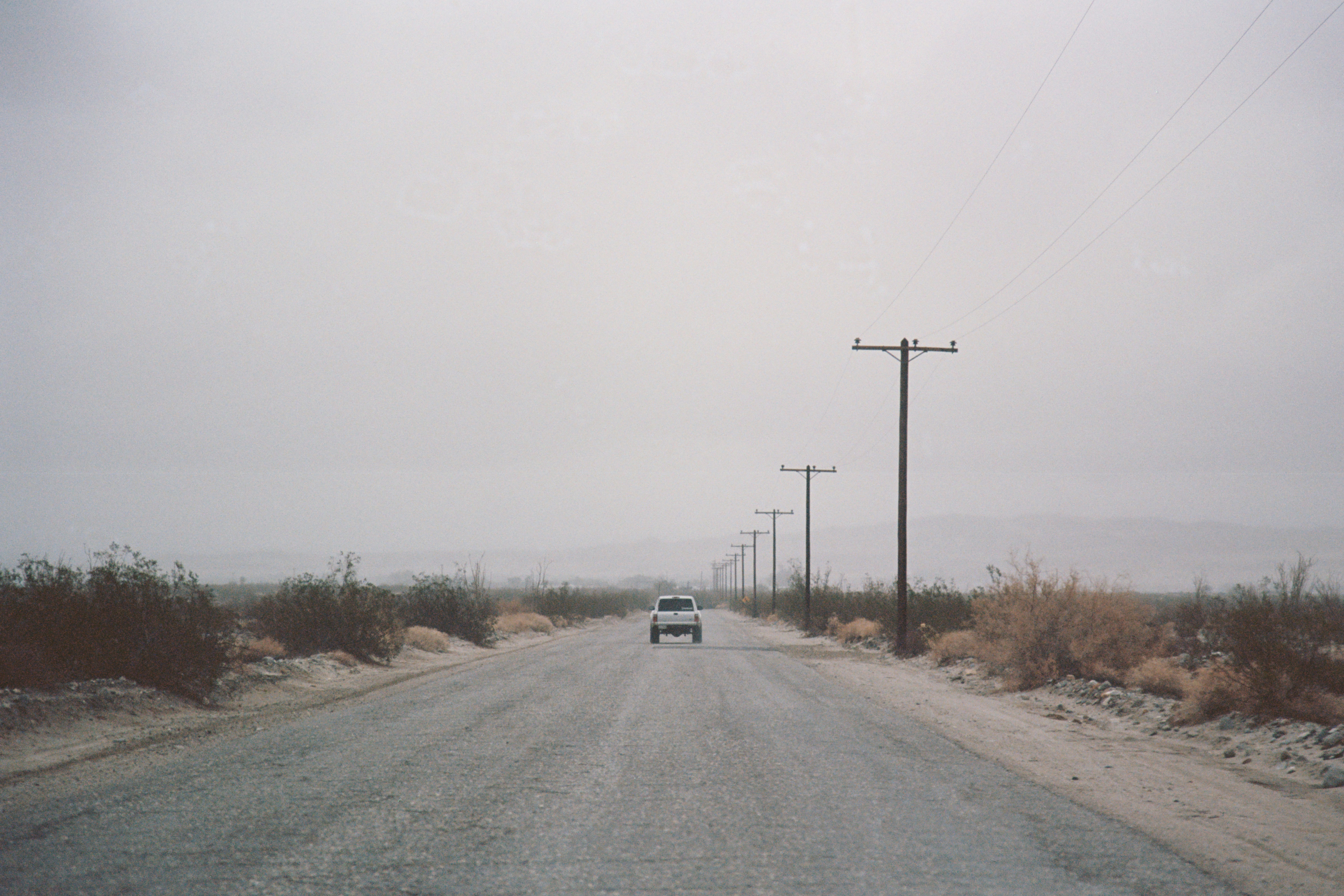 Hazy desert road with a car and utility poles