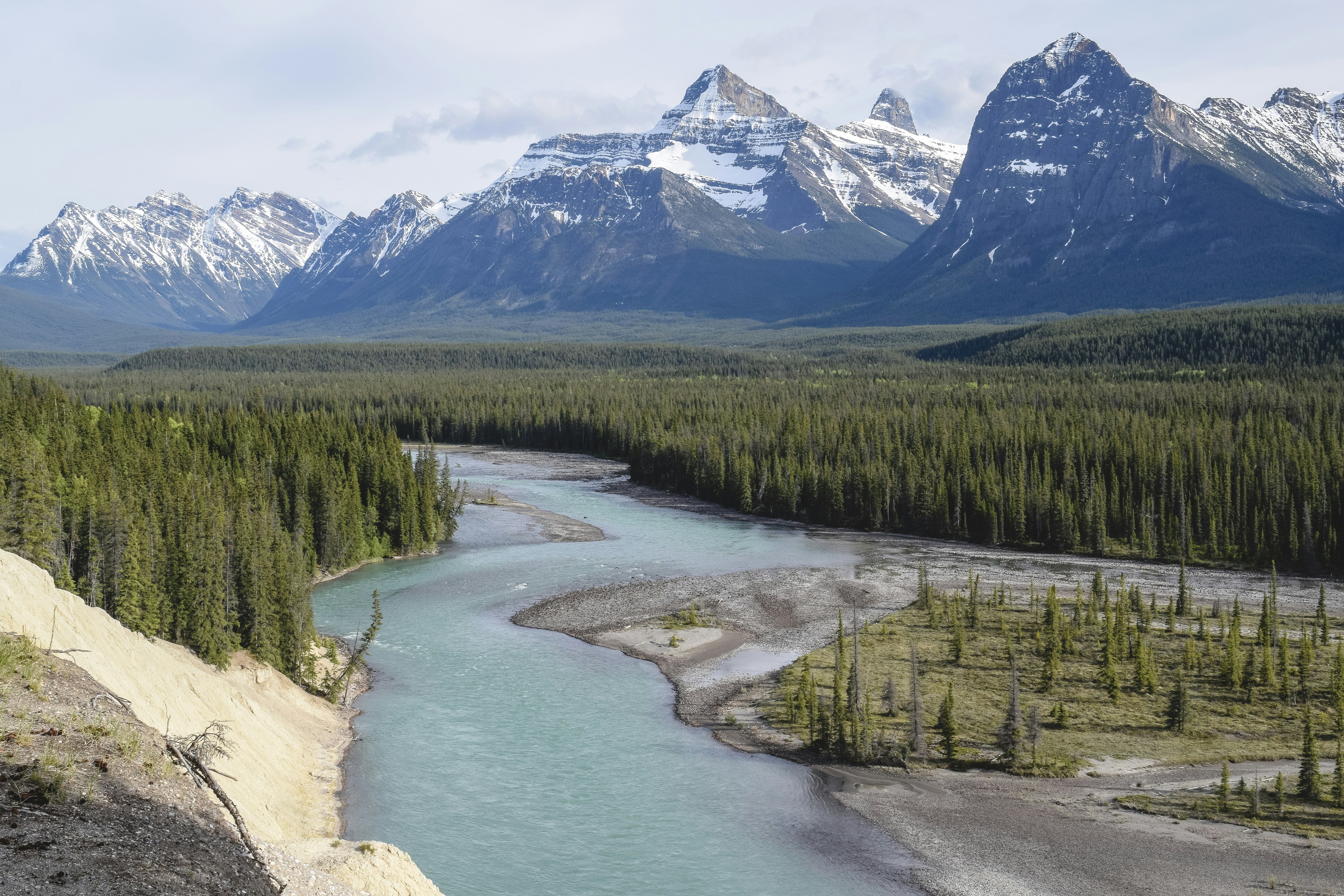 A winding river flows through a forest with snow-capped mountains