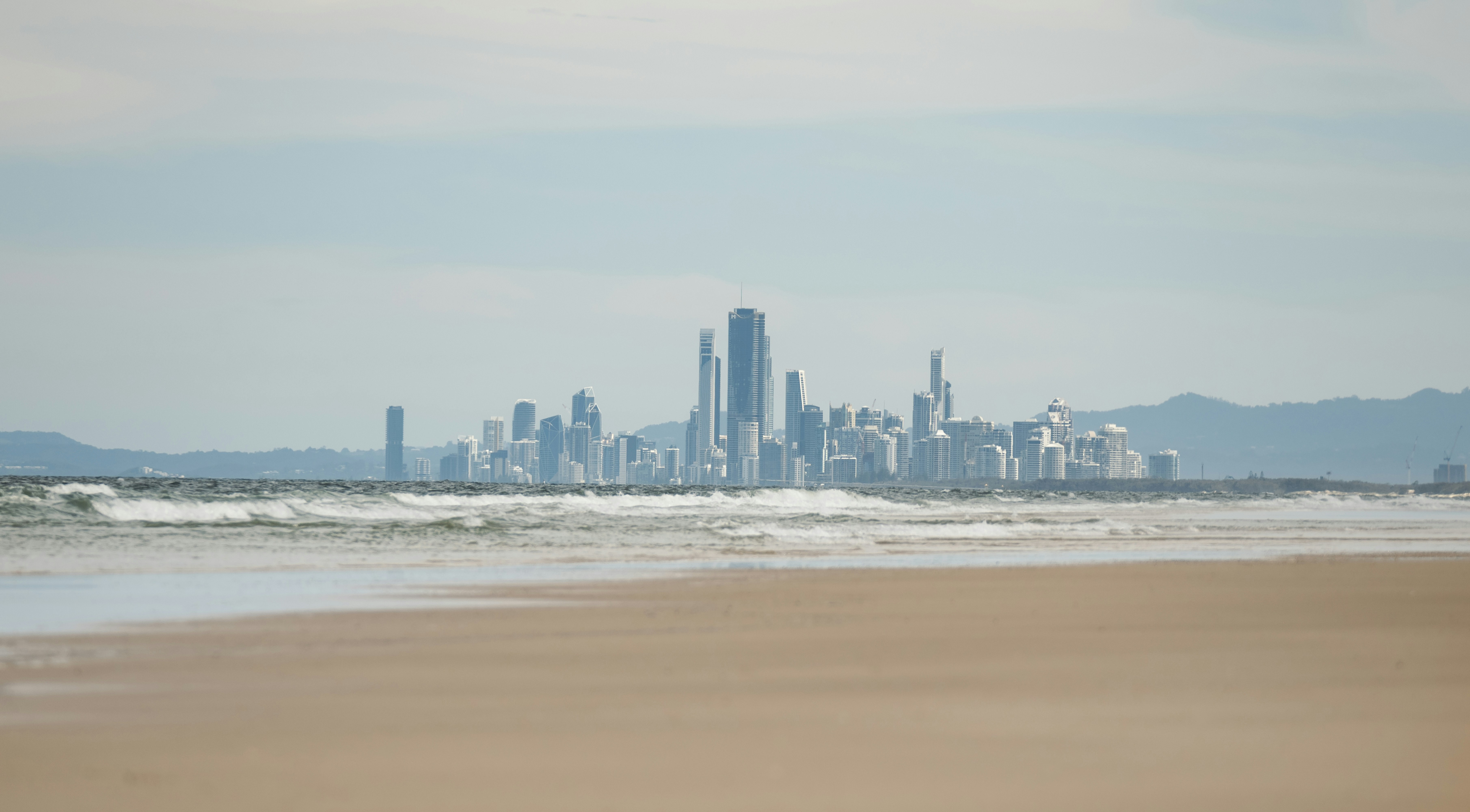Cityscape visible across a sandy beach and ocean waves