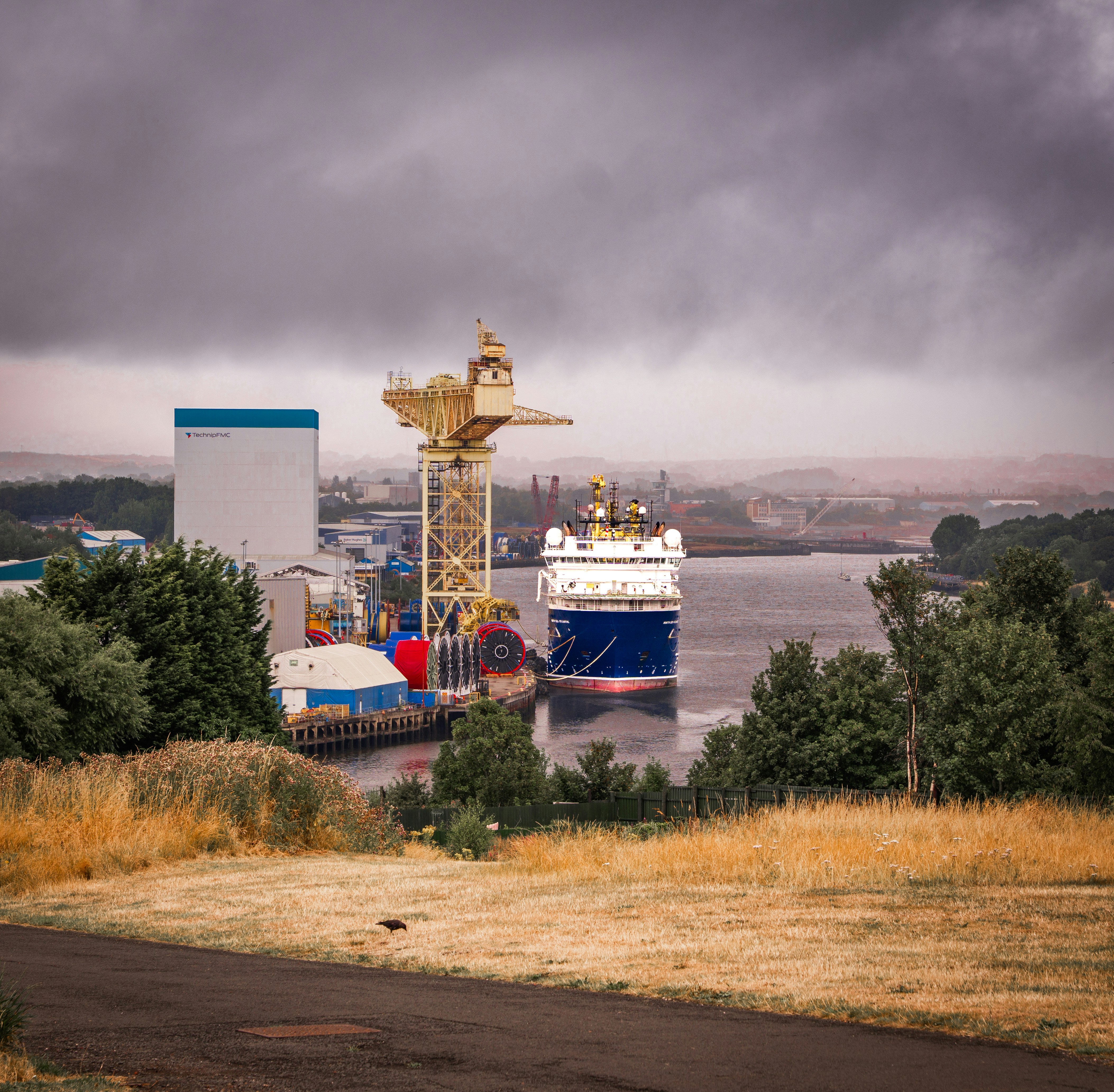 Industrial port with a ship, crane, and cloudy sky.