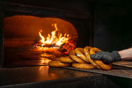 Hand placing simit into a traditional wood-fired oven