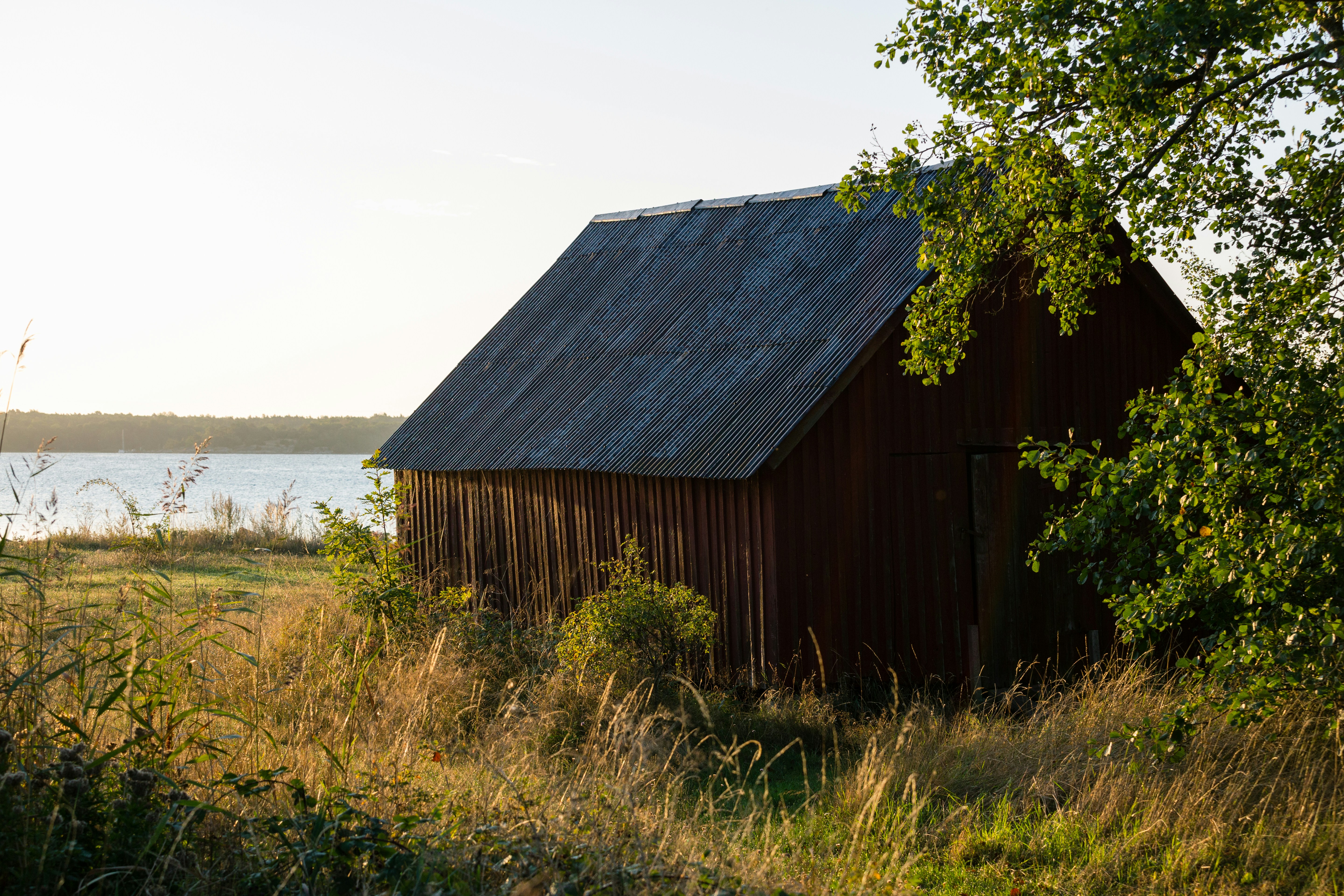 A rustic red barn stands by a lake at sunset