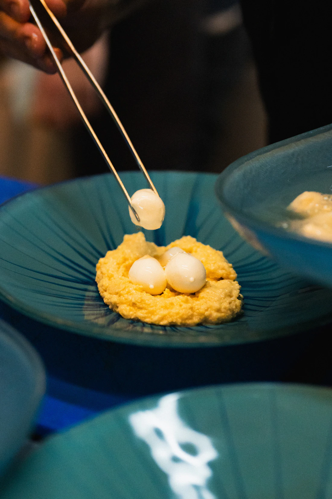 Tres quenelles blancas sobre crema amarilla en un plato azul