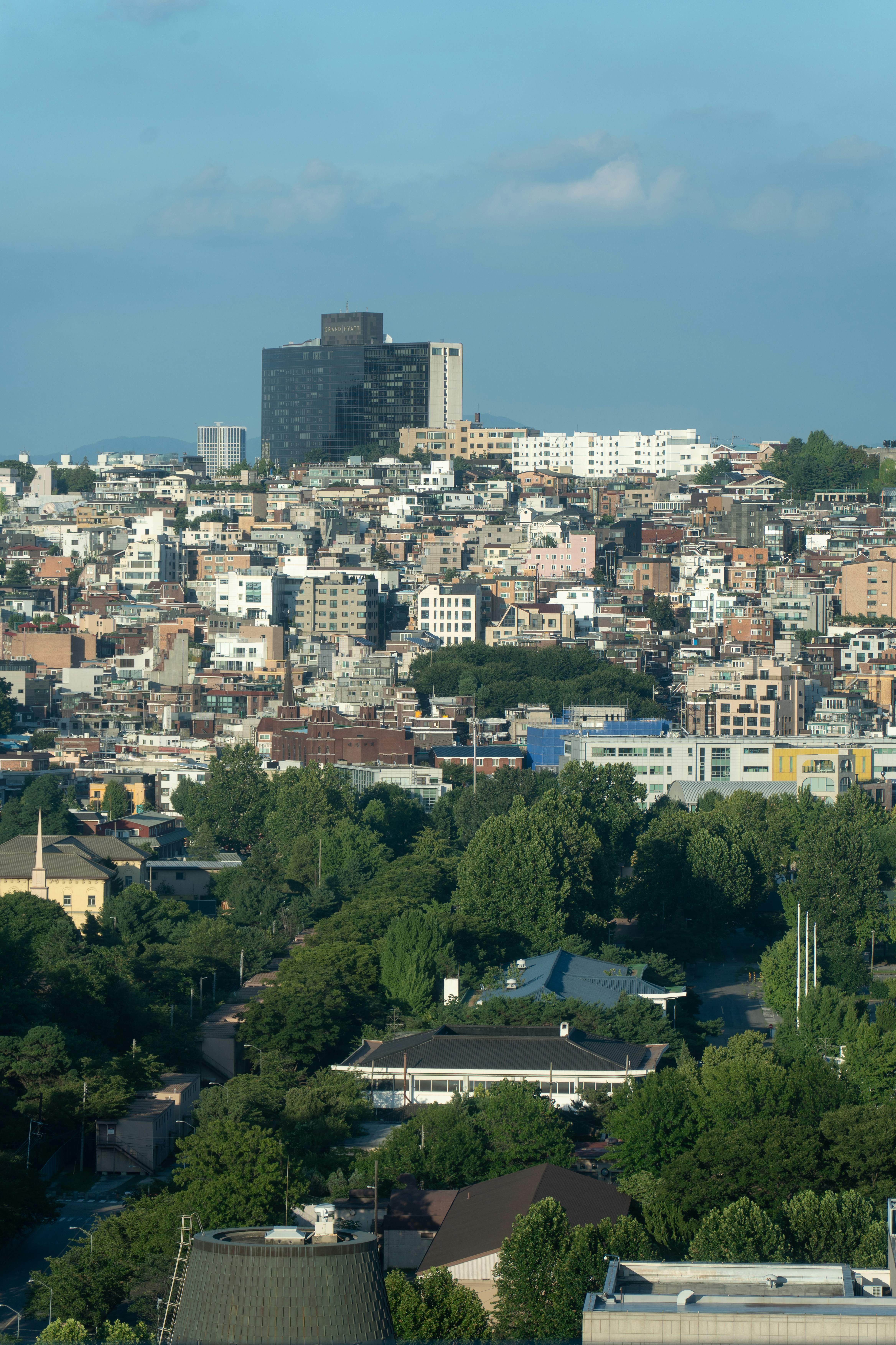 Urban landscape with buildings, green trees, and blue sky.