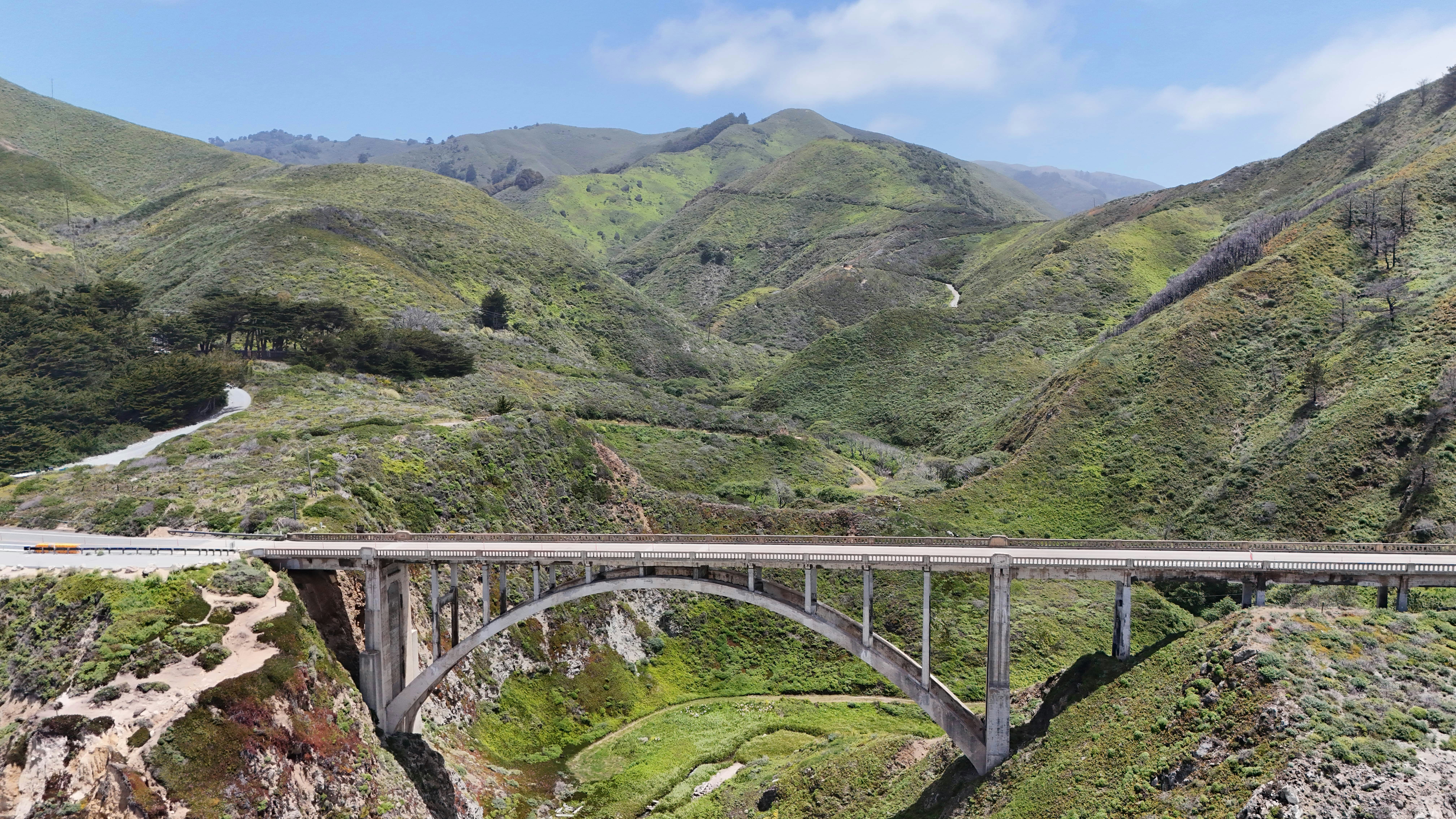 A concrete arch bridge spans a valley with green mountains - Free Photo ...