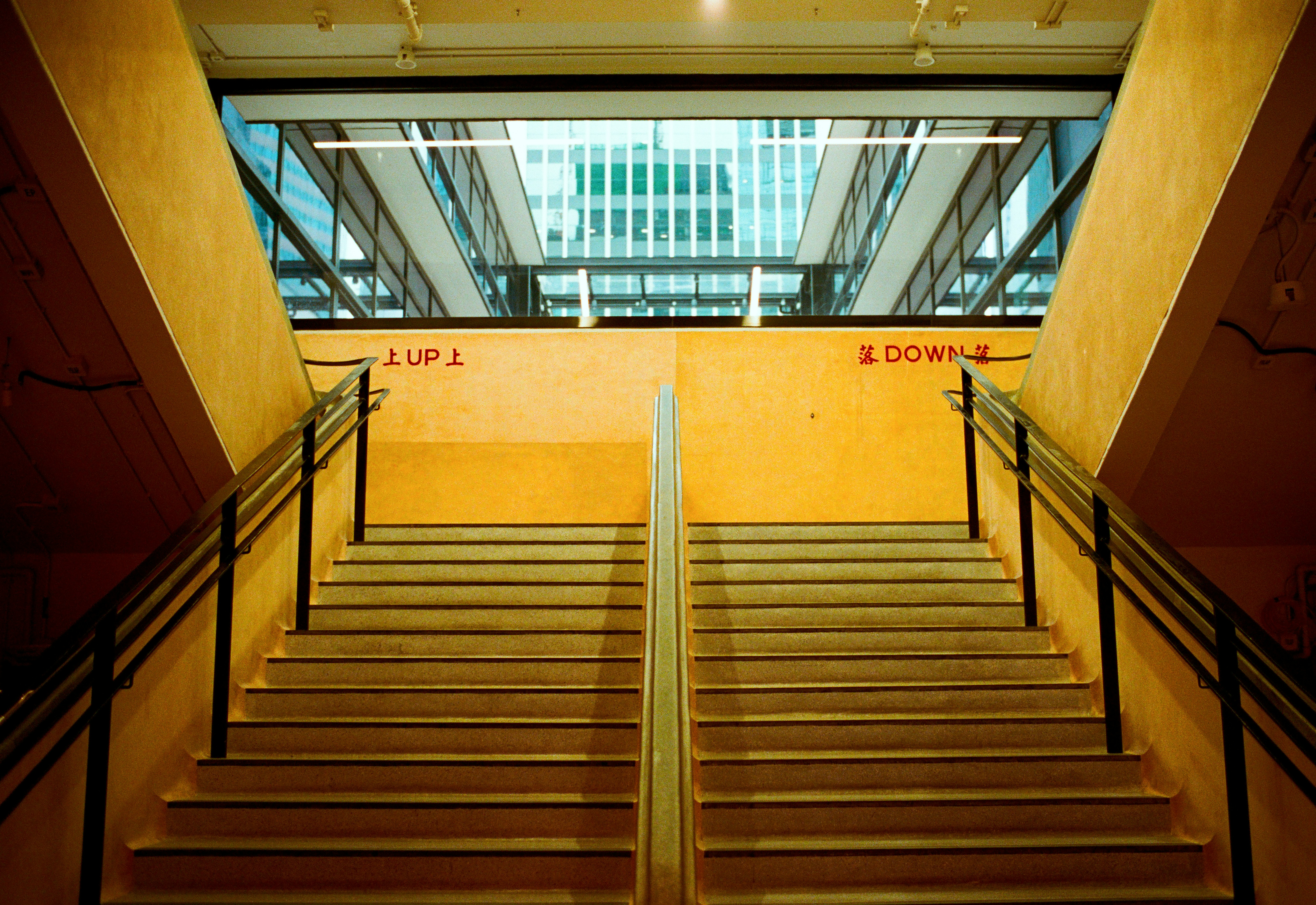 Symmetrical staircases lead to a yellow wall and glass ceiling
