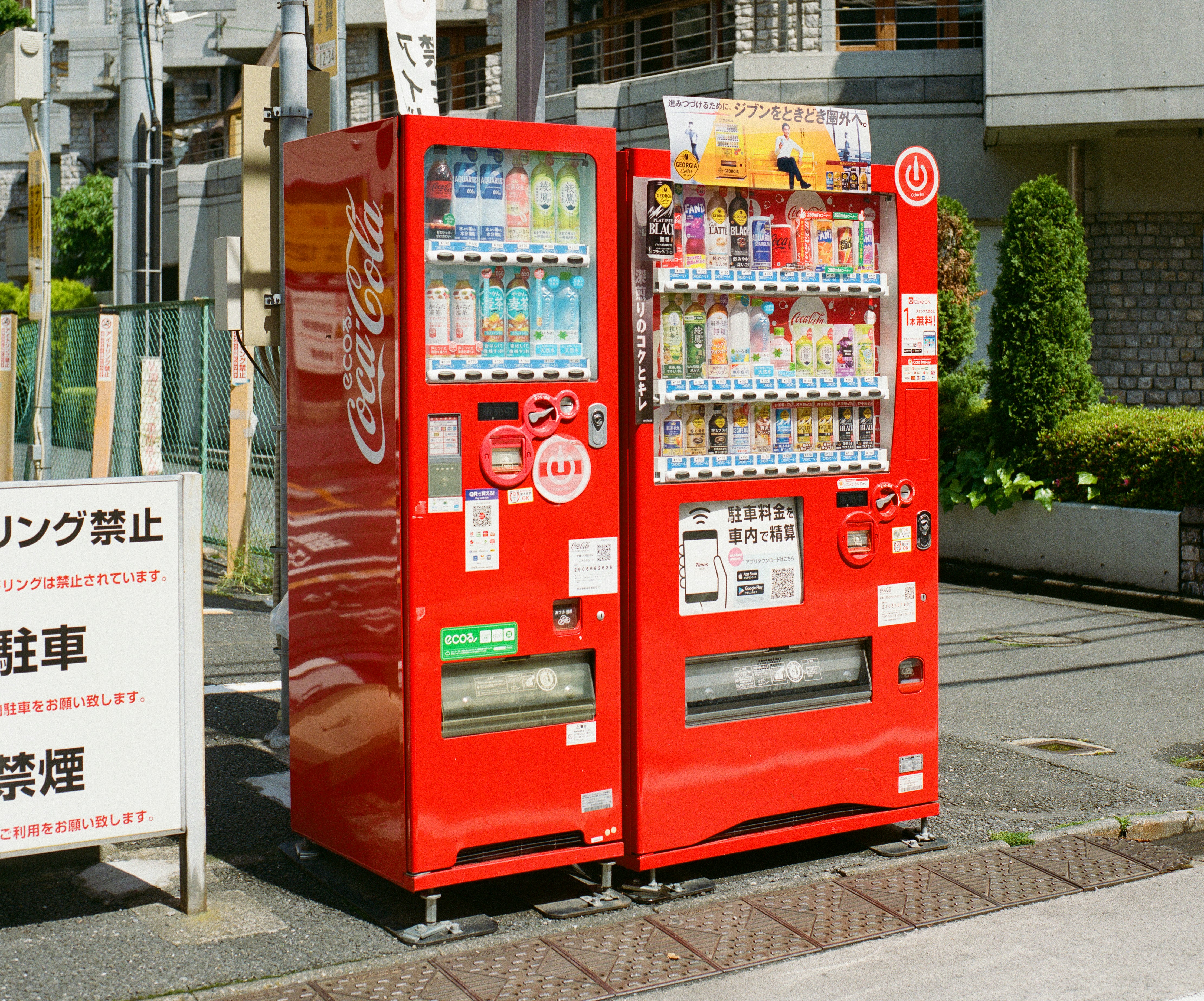 Two red vending machines stand on a city sidewalk