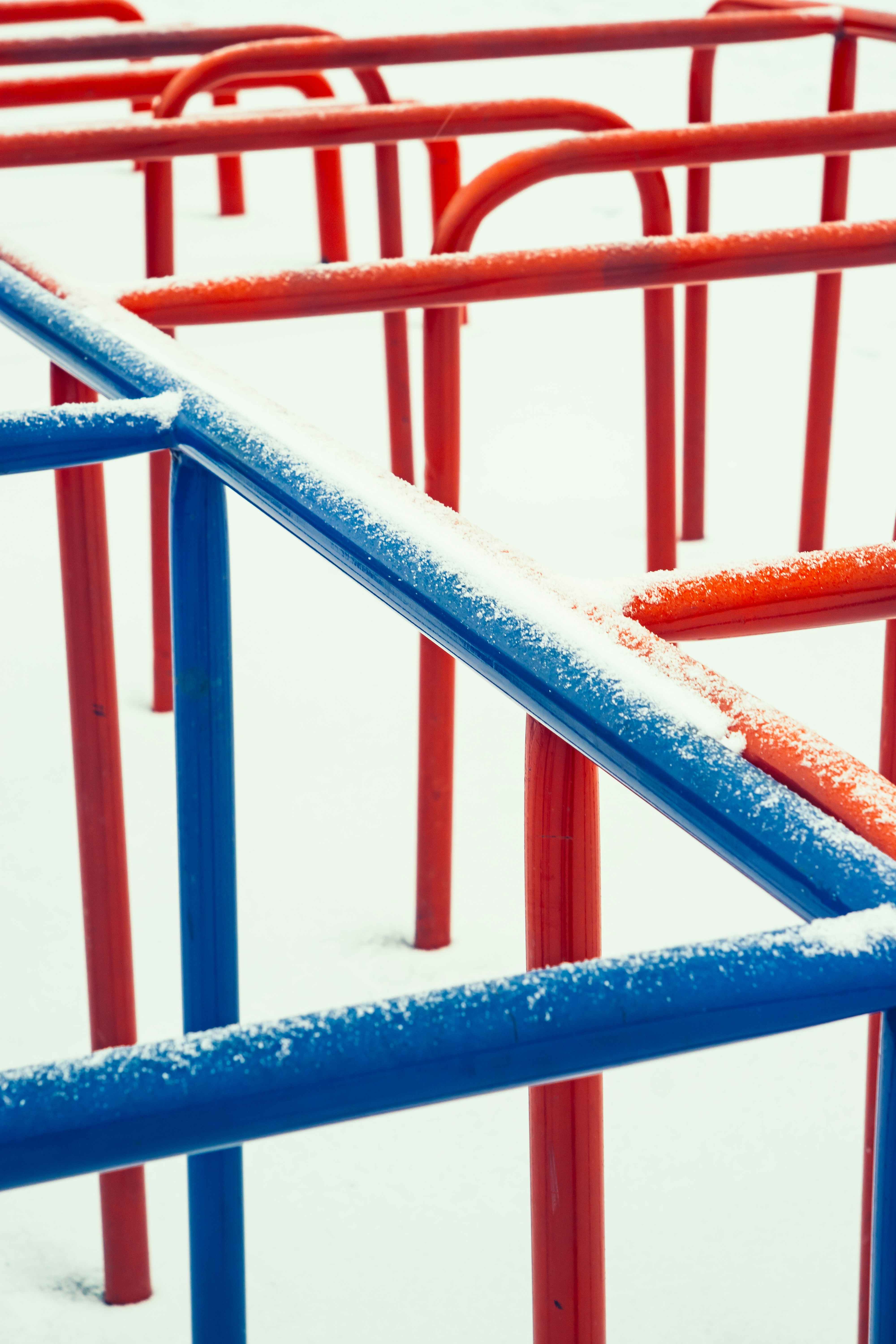 Snow covers red and blue playground monkey bars.