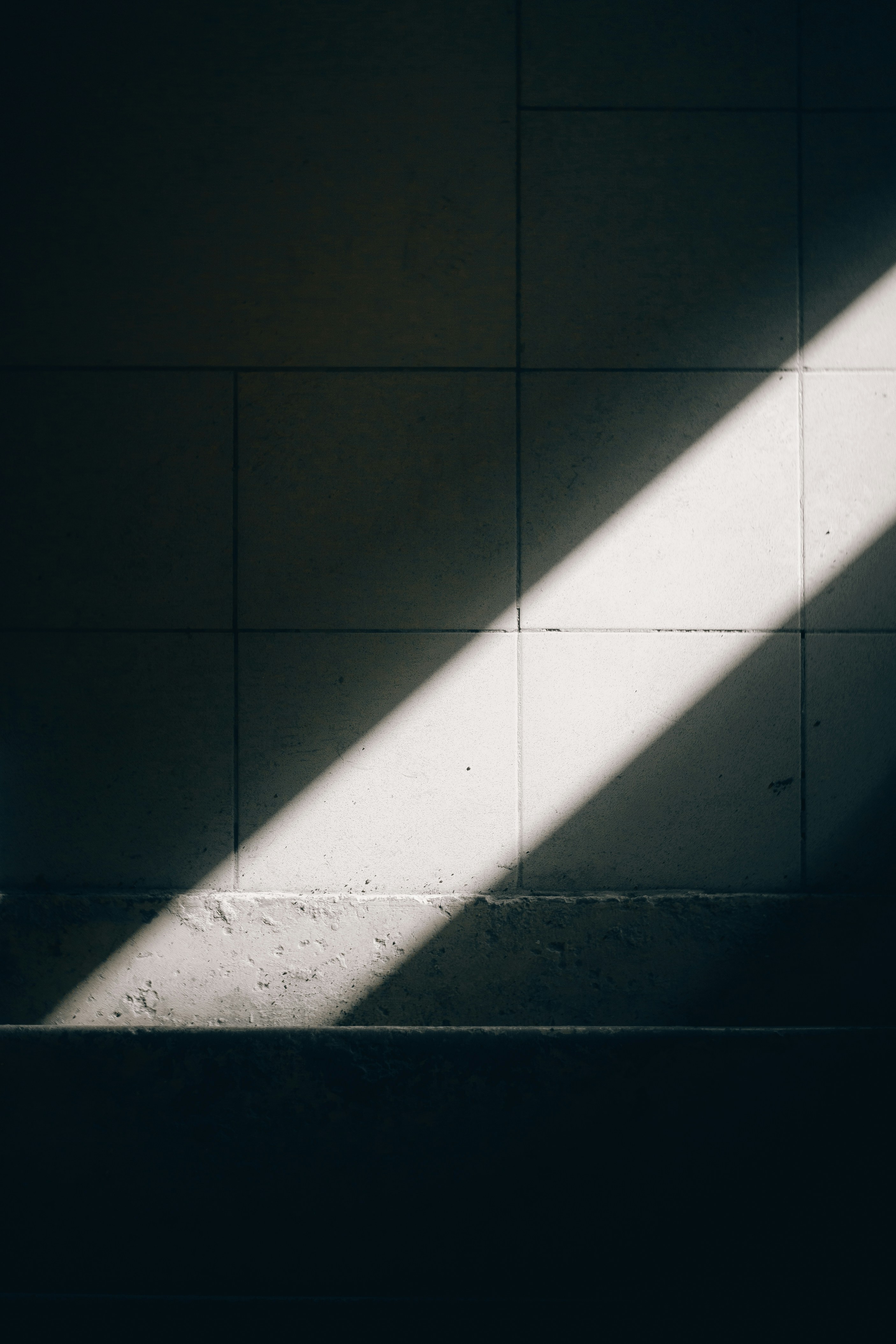 A diagonal beam of sunlight illuminates a tiled wall.