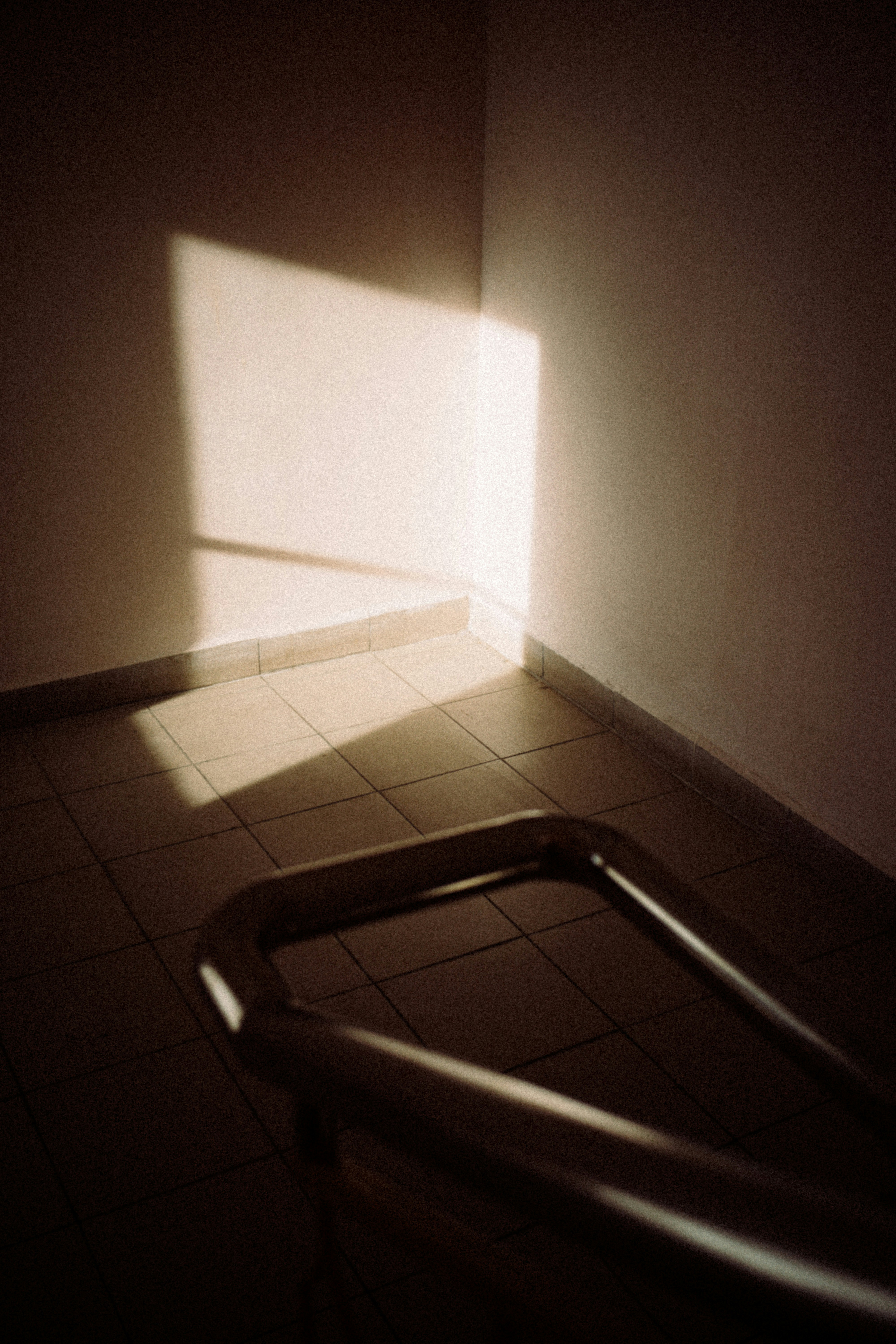 Sunlight on a corner wall, tiled floor, and metal railing.