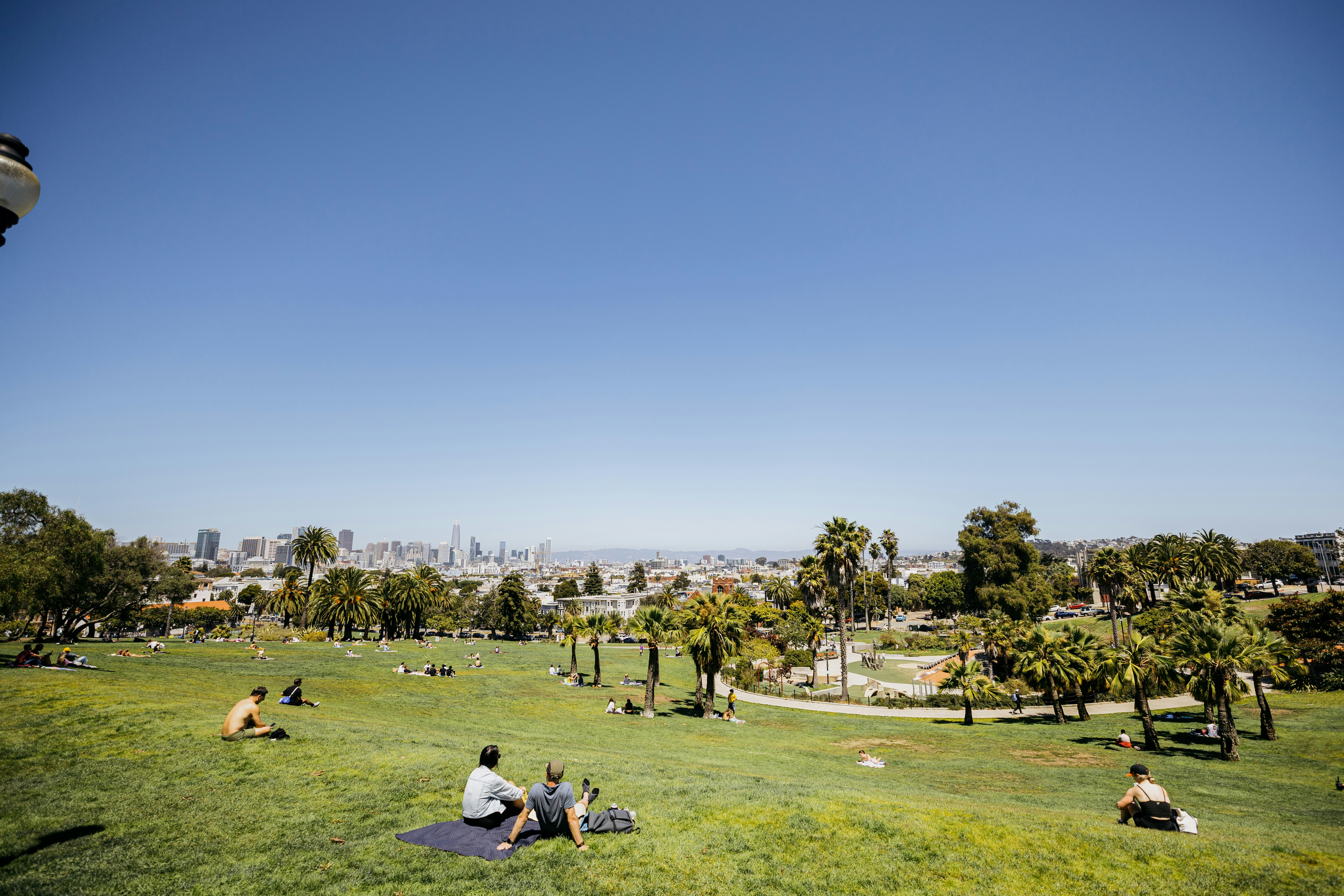 People relaxing in a sunny green park with city skyline.