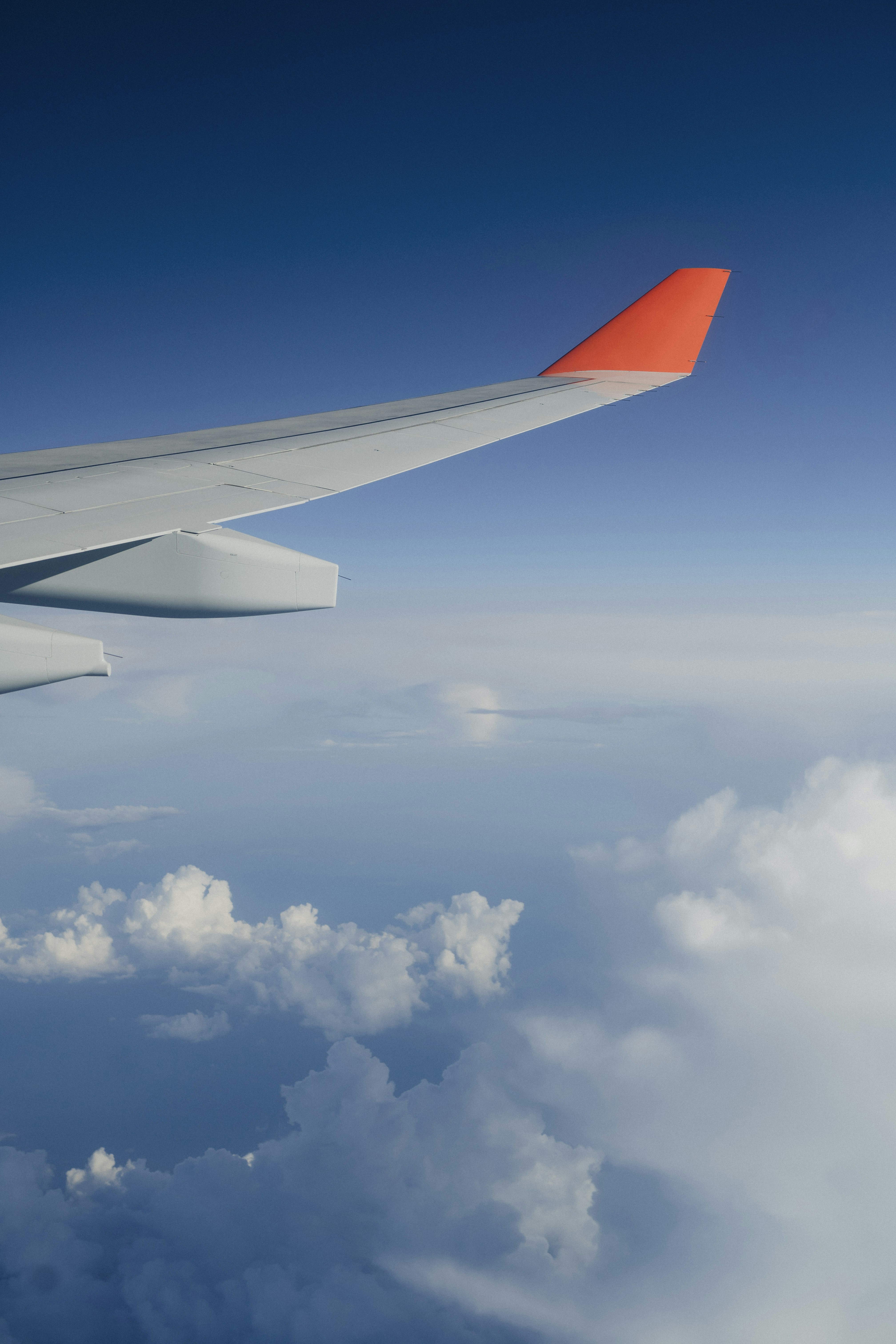 Airplane wing above white clouds and a blue sky.